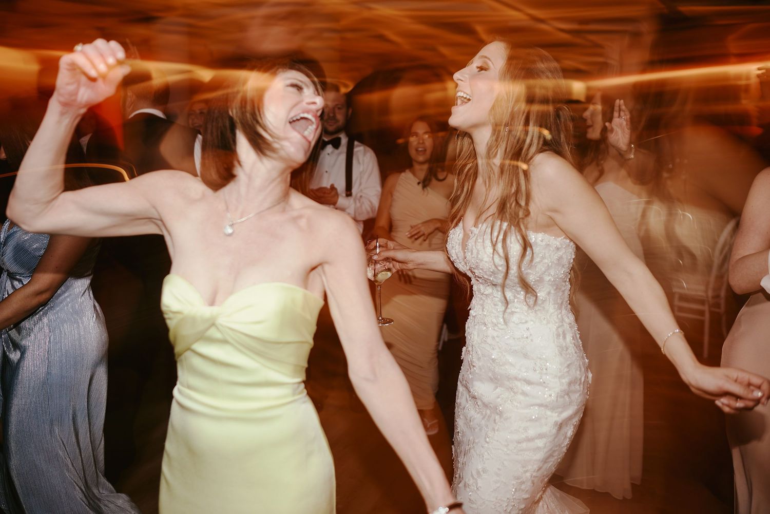 Wedding guests in formal attire dance energetically at a reception with motion blur effect creating a joyful atmosphere.