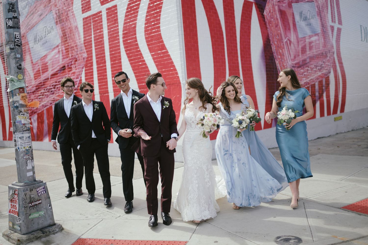 Wedding party in formal attire walking together against red and white wall backdrop.