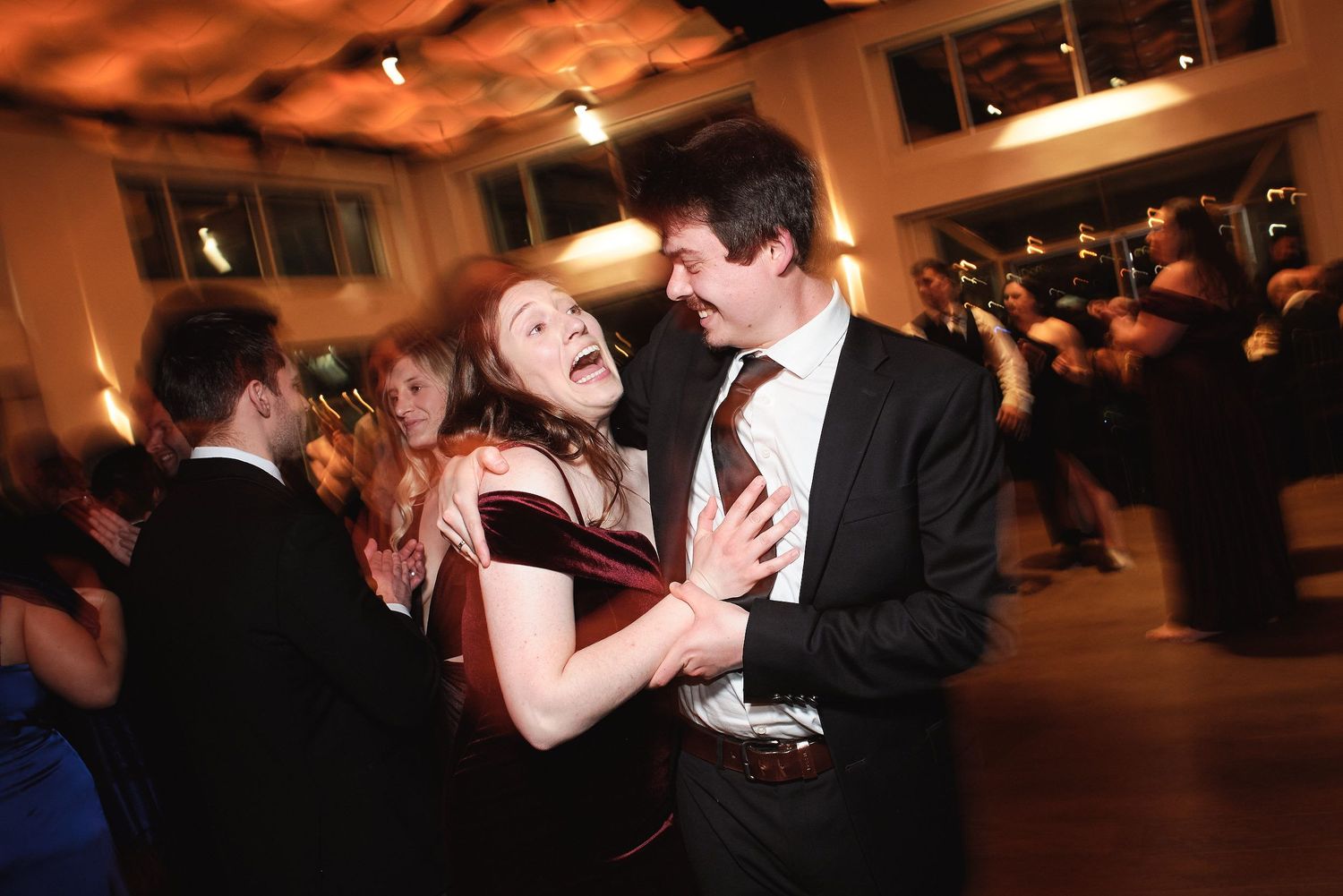 Formal couple dancing together at an evening event with a warm amber glow in the reception hall.