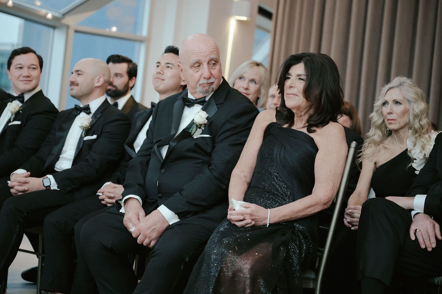 Wedding party members in formal black attire seated in a row during ceremony.