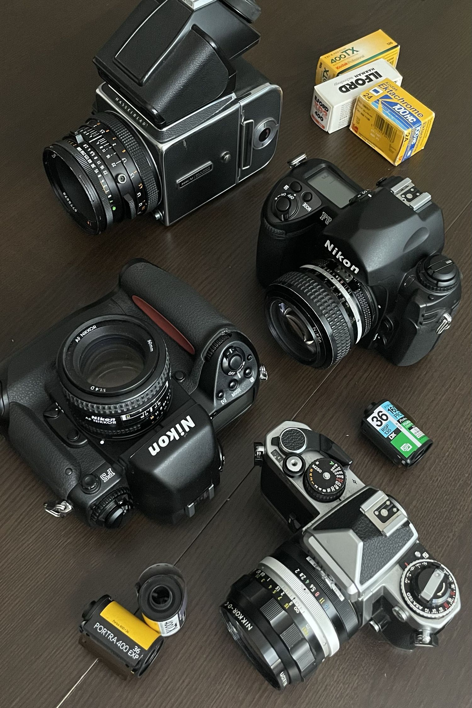Collection of vintage and modern cameras including Nikon and Hasselblad models displayed with film canisters on dark surface.