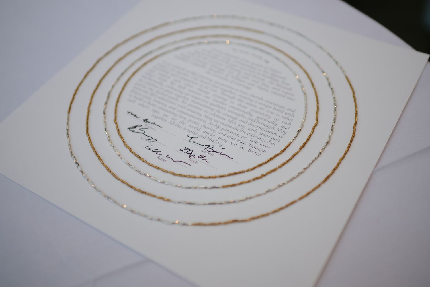 A wedding ketubah document features elegant gold circular patterns around handwritten text and signatures.