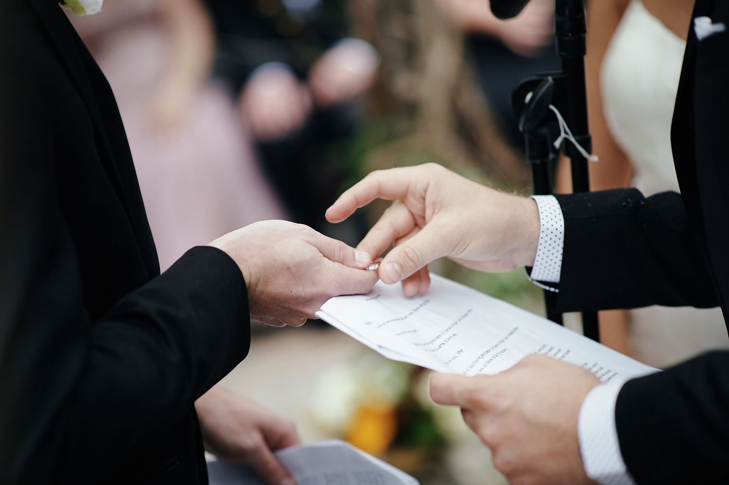 Close-up shot of hands exchanging wedding papers during an outdoor ceremony.