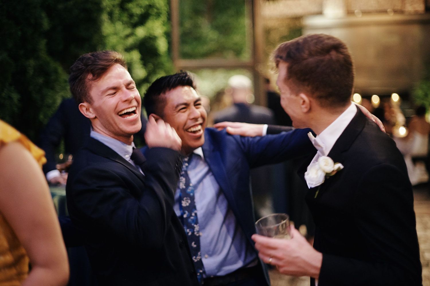 Wedding guests sharing laughs and drinks during outdoor evening reception.
