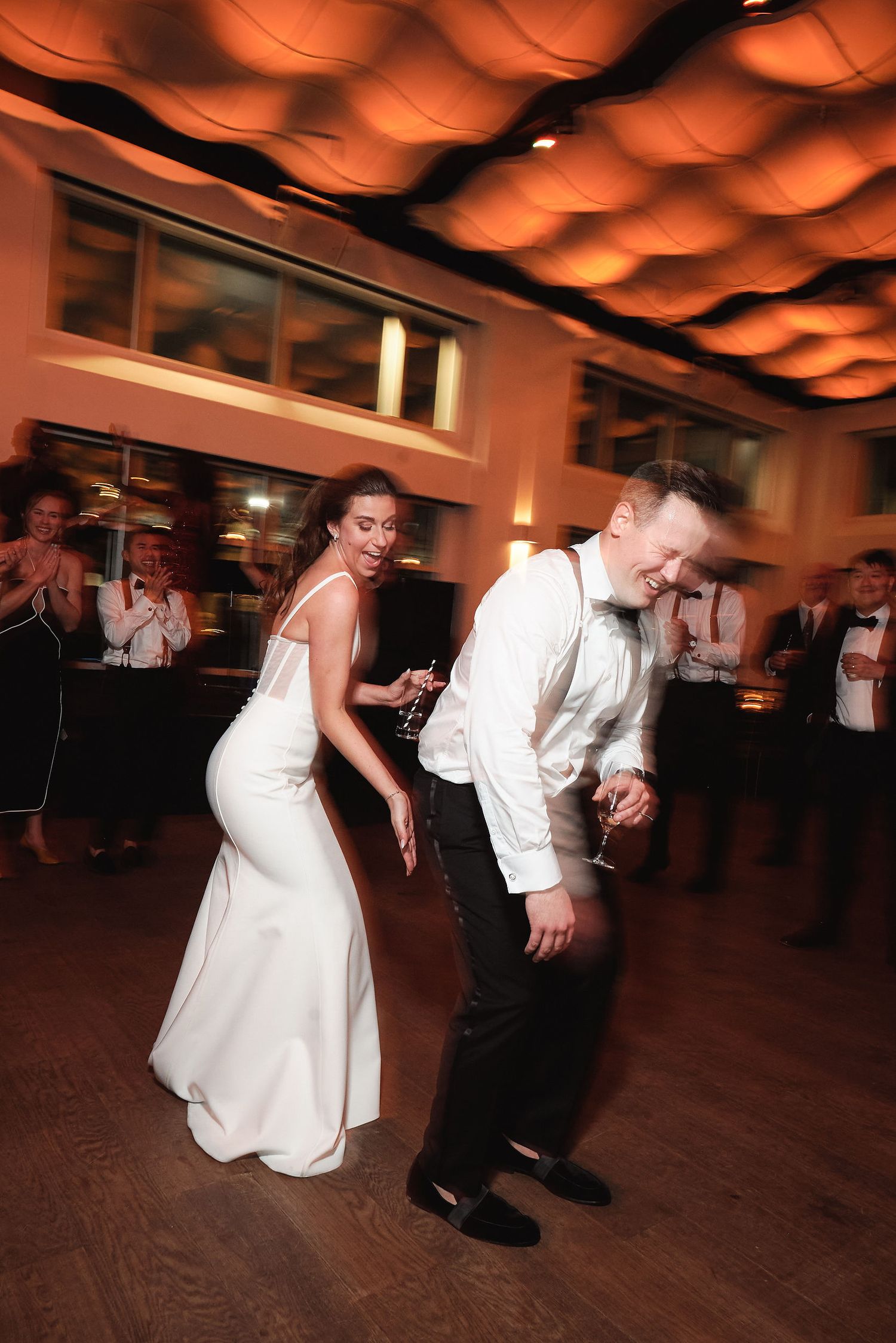 Couple on the dance floor at wedding reception with warm orange lighting and decorative ceiling details overhead.