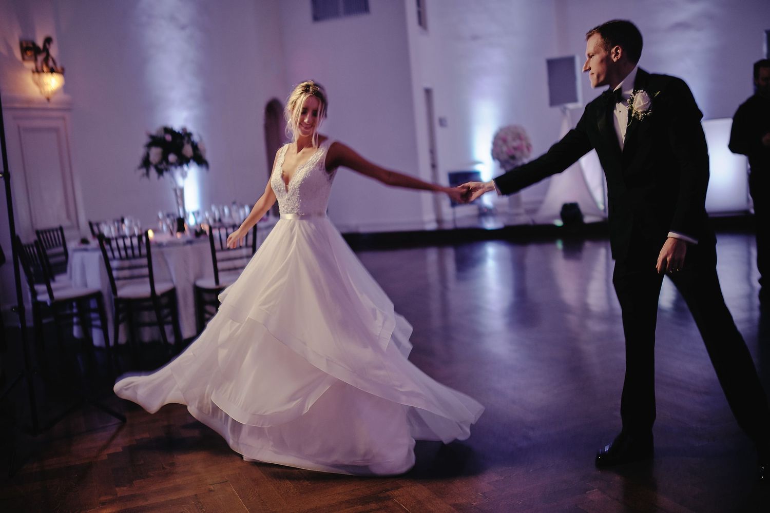Couple dancing at wedding reception as bride's white gown twirls elegantly across dark ballroom floor.