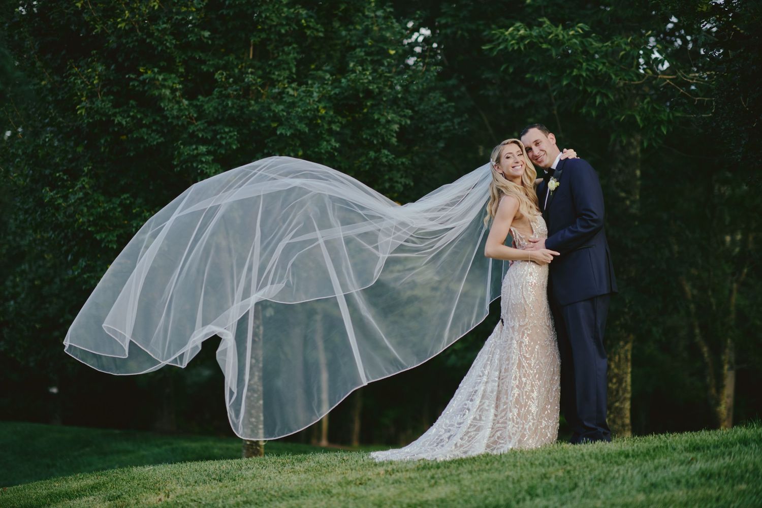 A bride and groom share a romantic moment outdoors as her long veil flows dramatically in the wind.