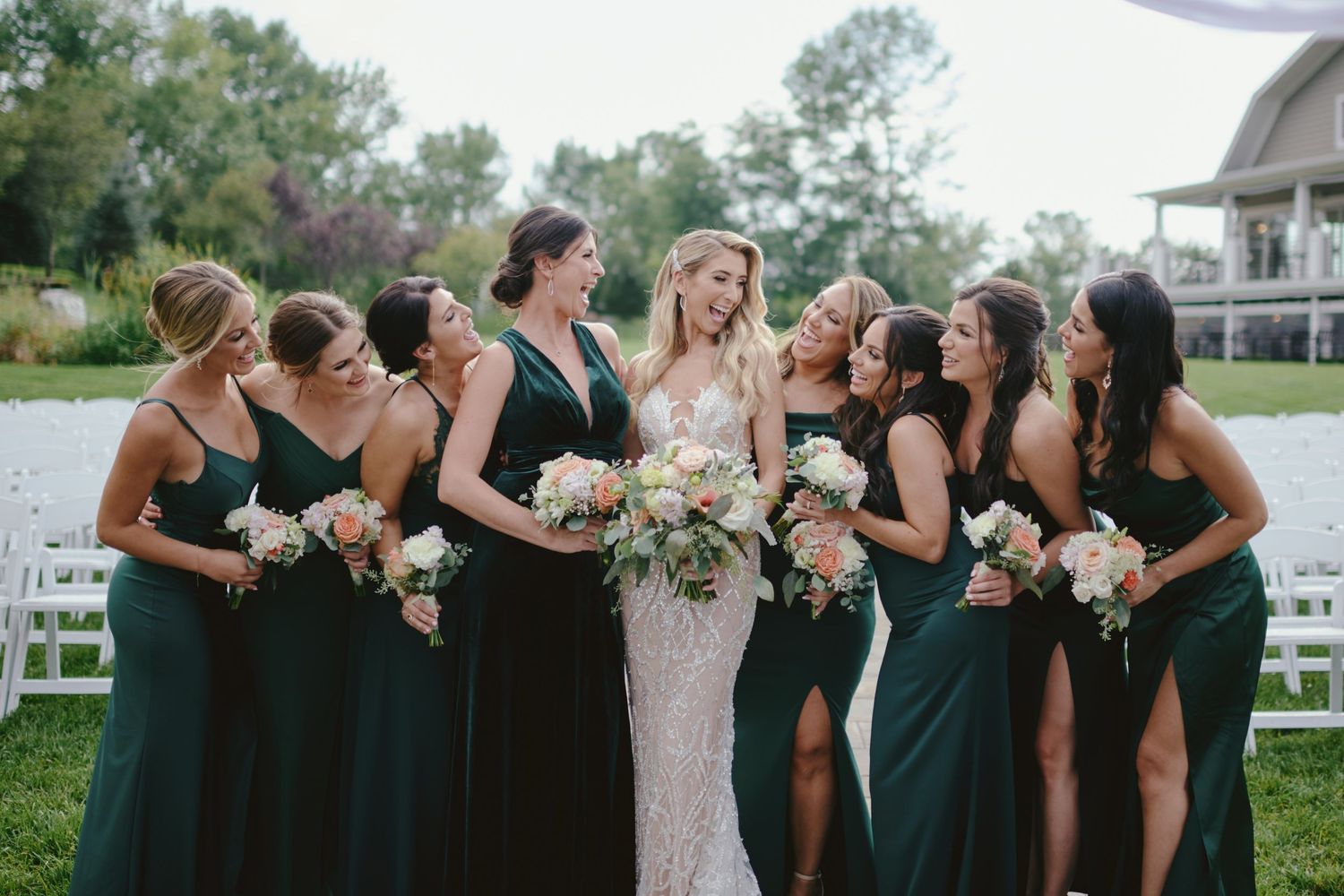 Bridesmaids wearing elegant emerald green dresses pose with the bride in white at an outdoor garden wedding ceremony.