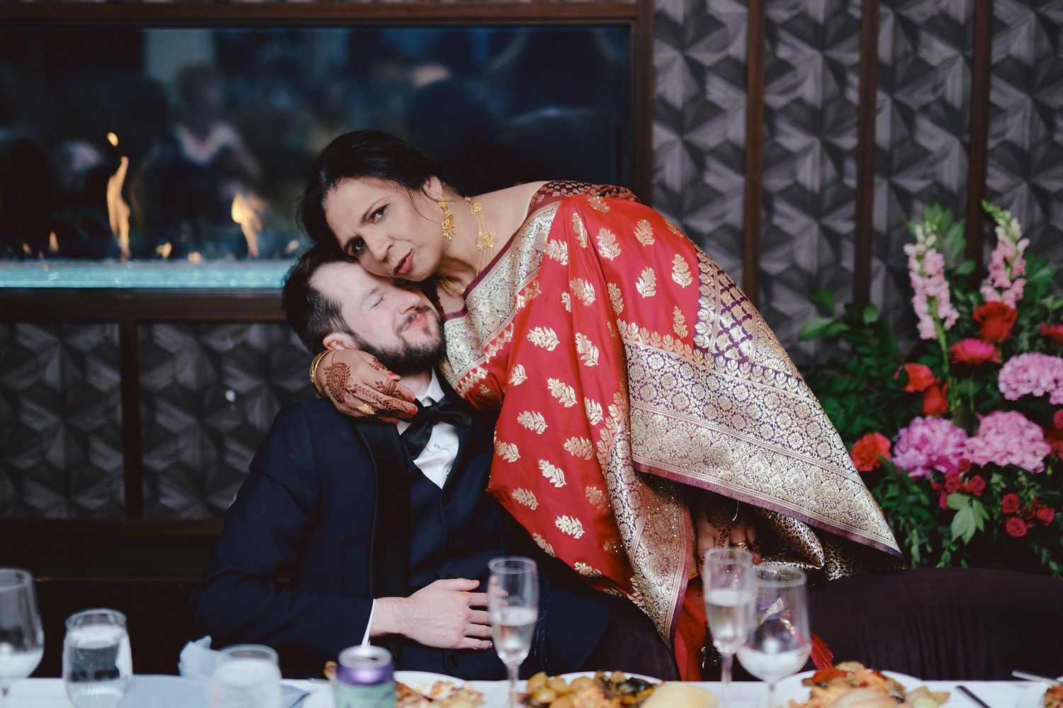 A tender romantic moment shared between two people at a restaurant table with candles and flowers in the background.