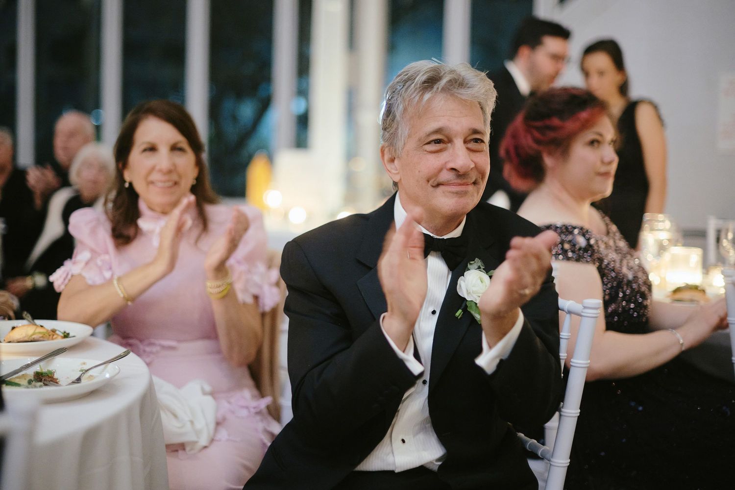 Wedding guests enjoying and applauding during a reception dinner in formal evening attire.