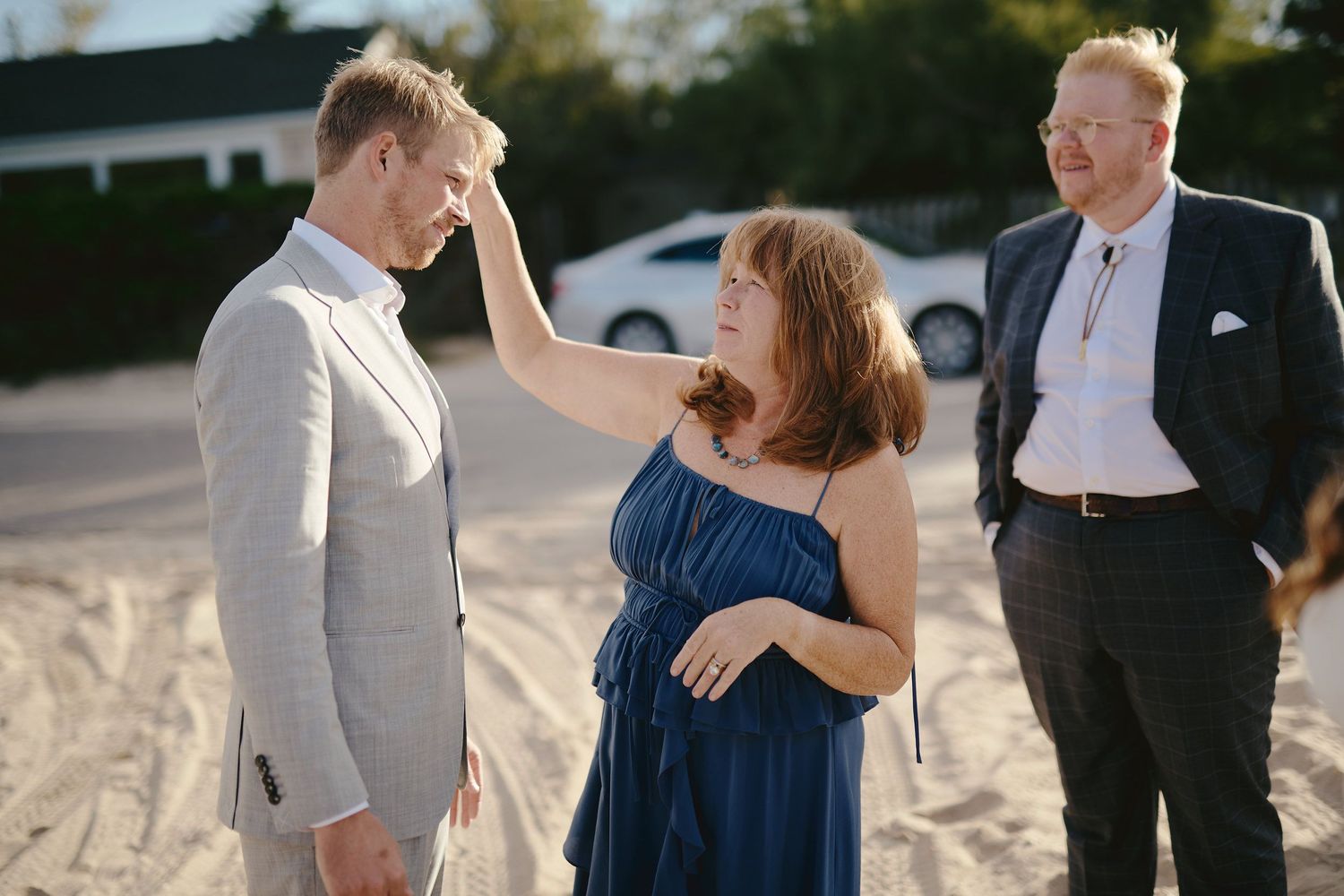 Three people share a cheerful moment on a sandy beach, with one in a navy dress gesturing playfully.