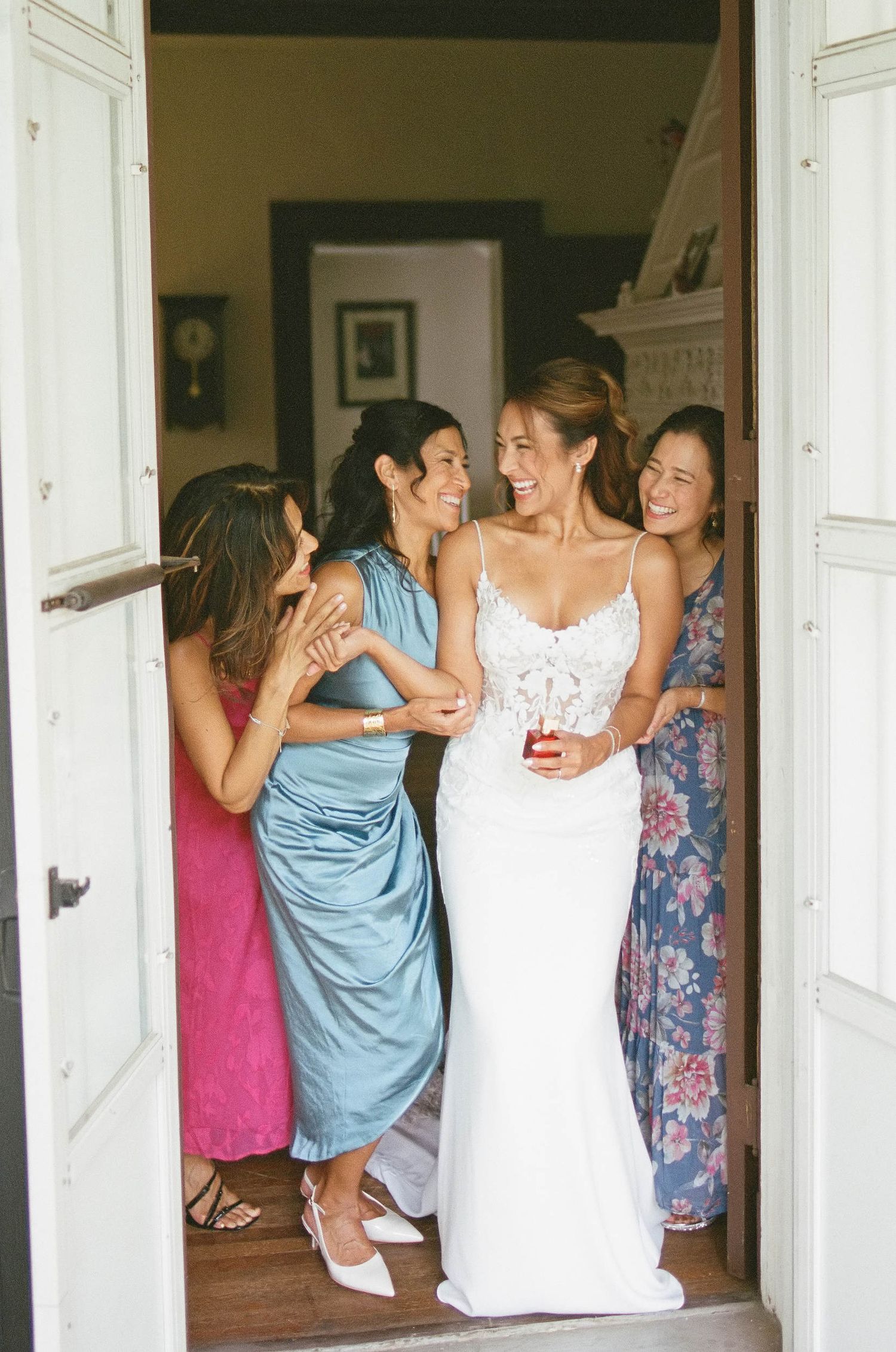 A group of women in colorful dresses share a joyful moment in a doorway during a special occasion.