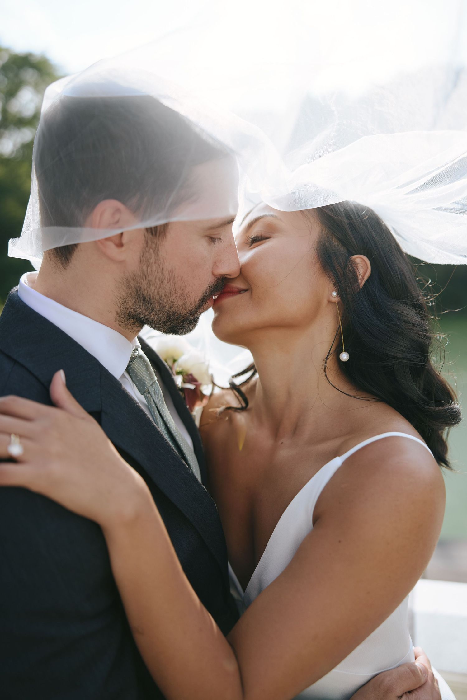 Bride and groom sharing a romantic kiss under a flowing white veil on their wedding day.