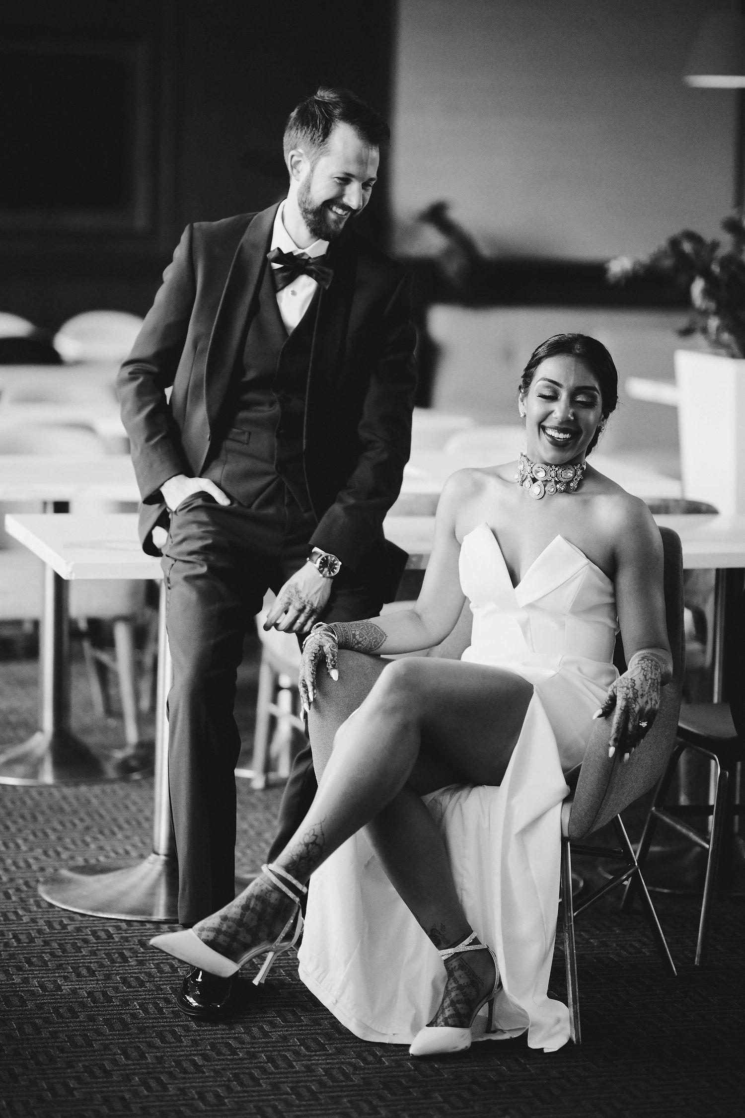 Black and white candid wedding reception photo shows couple sharing laughter in formal attire.