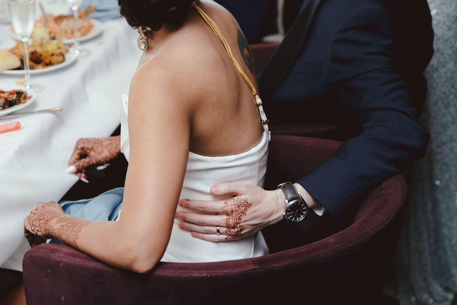 Close-up view of two people sitting close at a wedding reception dinner table with white linens and place settings.
