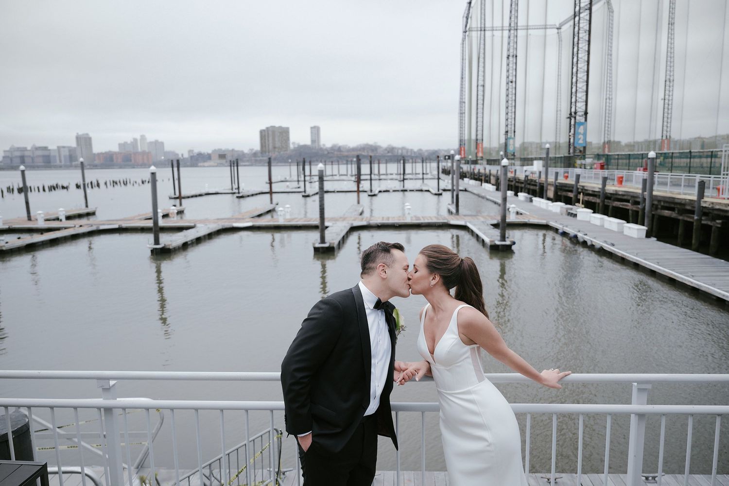 A couple shares a romantic moment at a misty marina with boats and docks in the background.