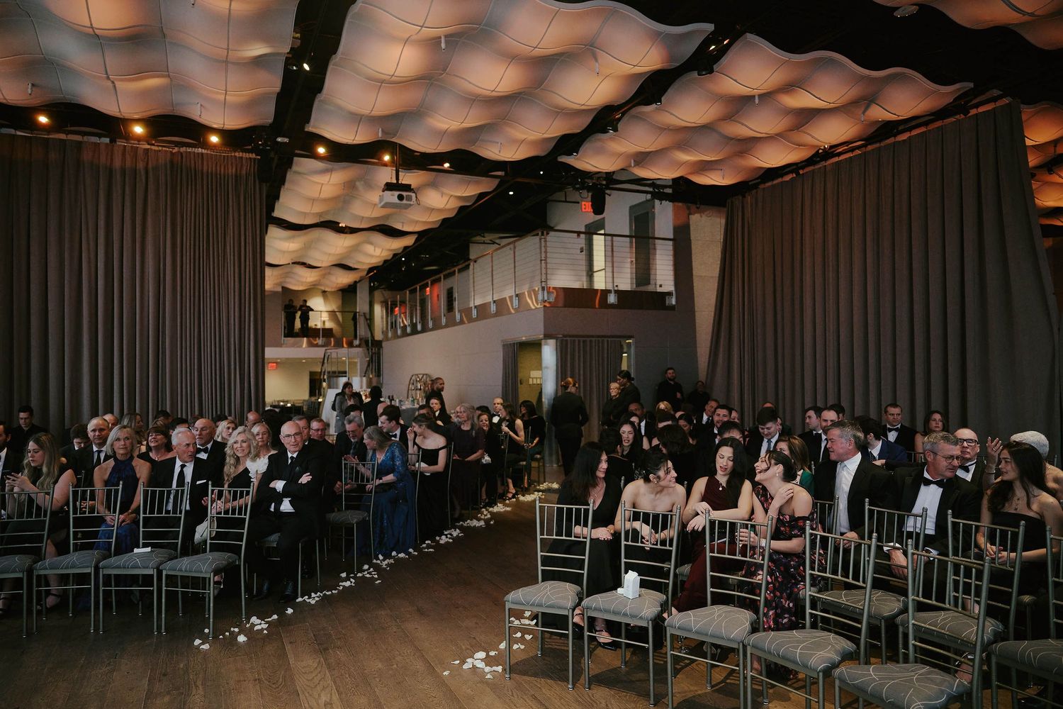 Wedding ceremony venue with dramatic draped ceiling and rows of silver chiavari chairs filled with guests.