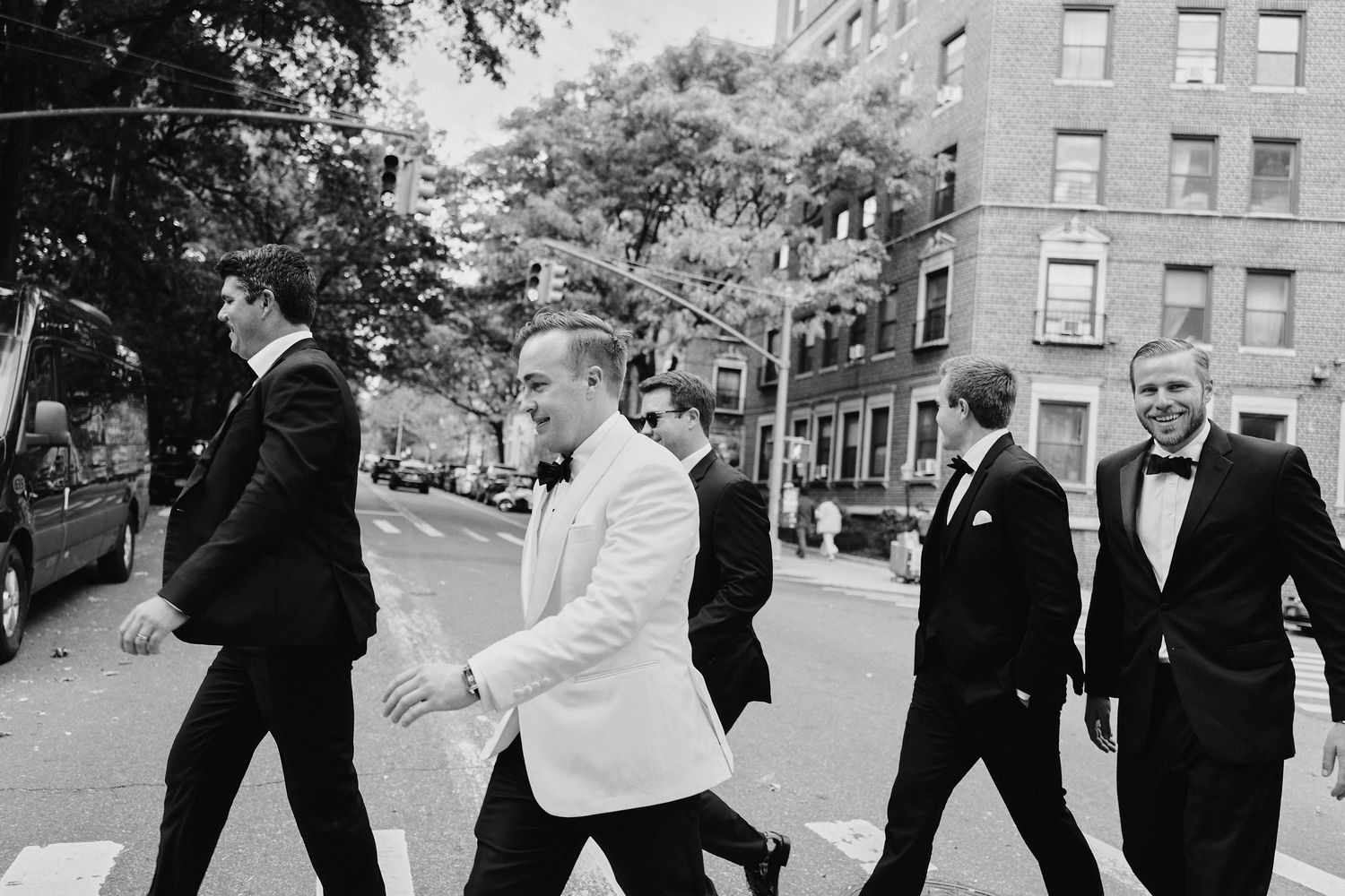 Black and white photo of groomsmen in tuxedos walking down a city street on a wedding day.