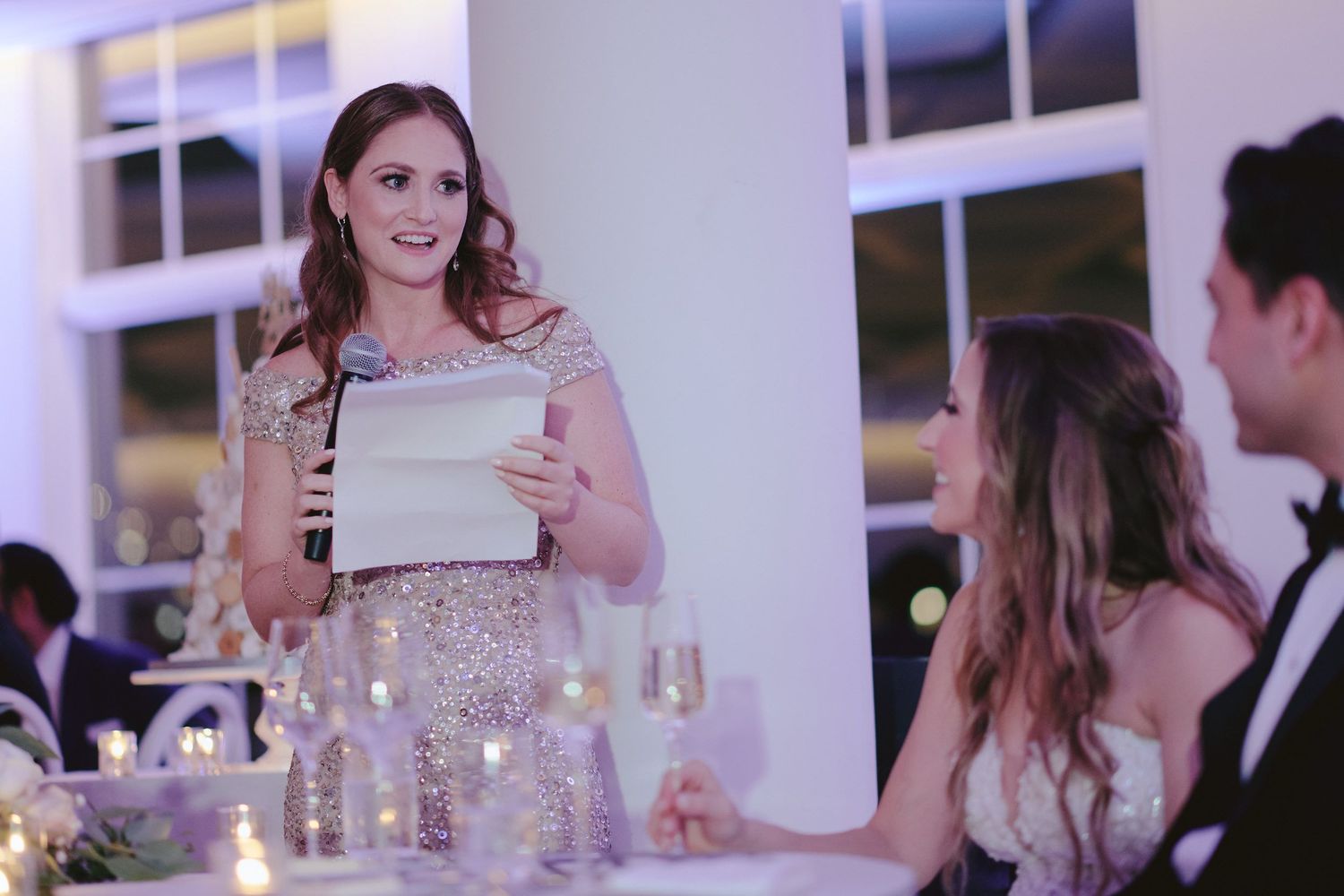Person giving a speech at an elegant reception with glowing candles and formal table settings.