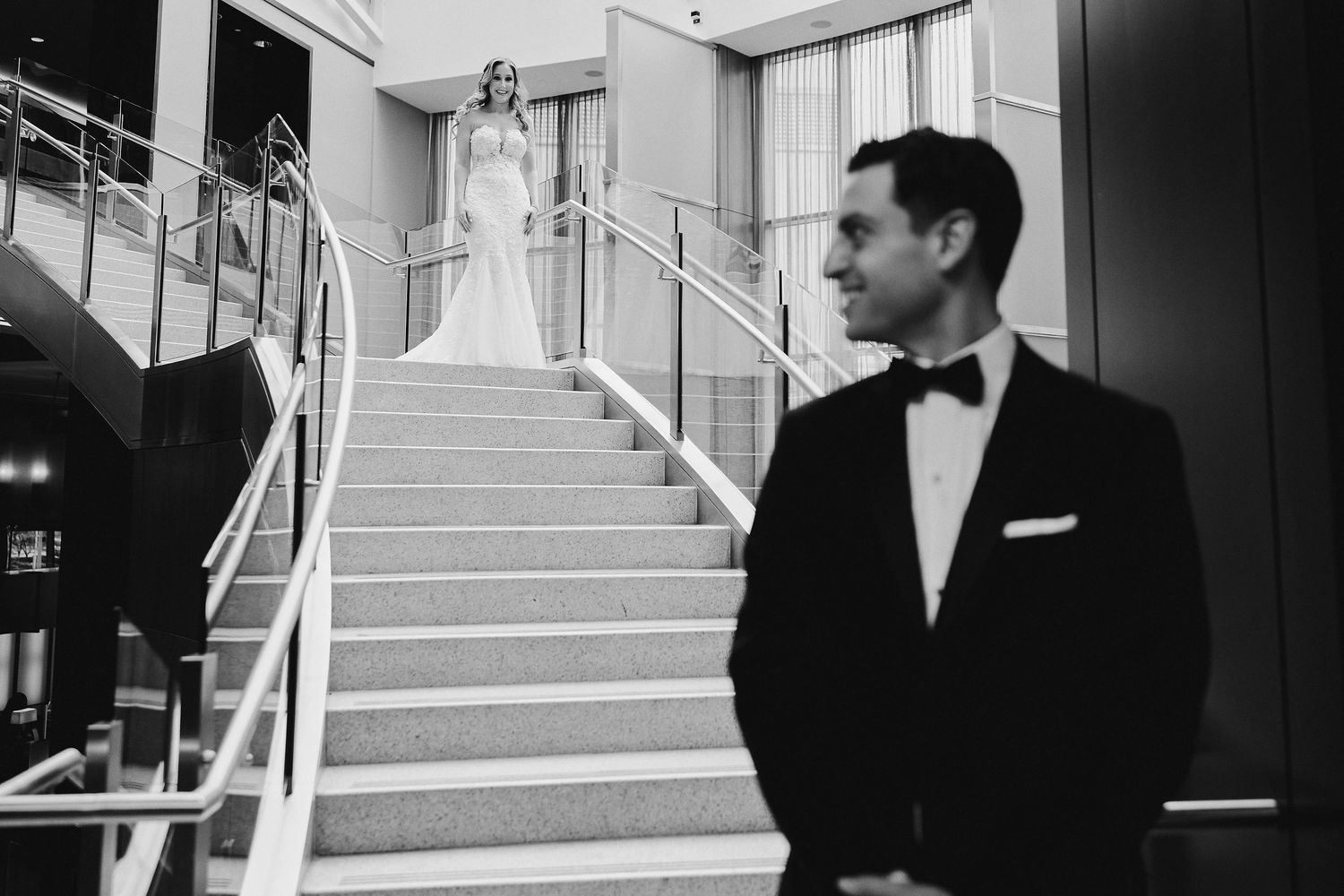 A stylish black and white photo showing a wedding couple on grand interior stairs in a classic venue.