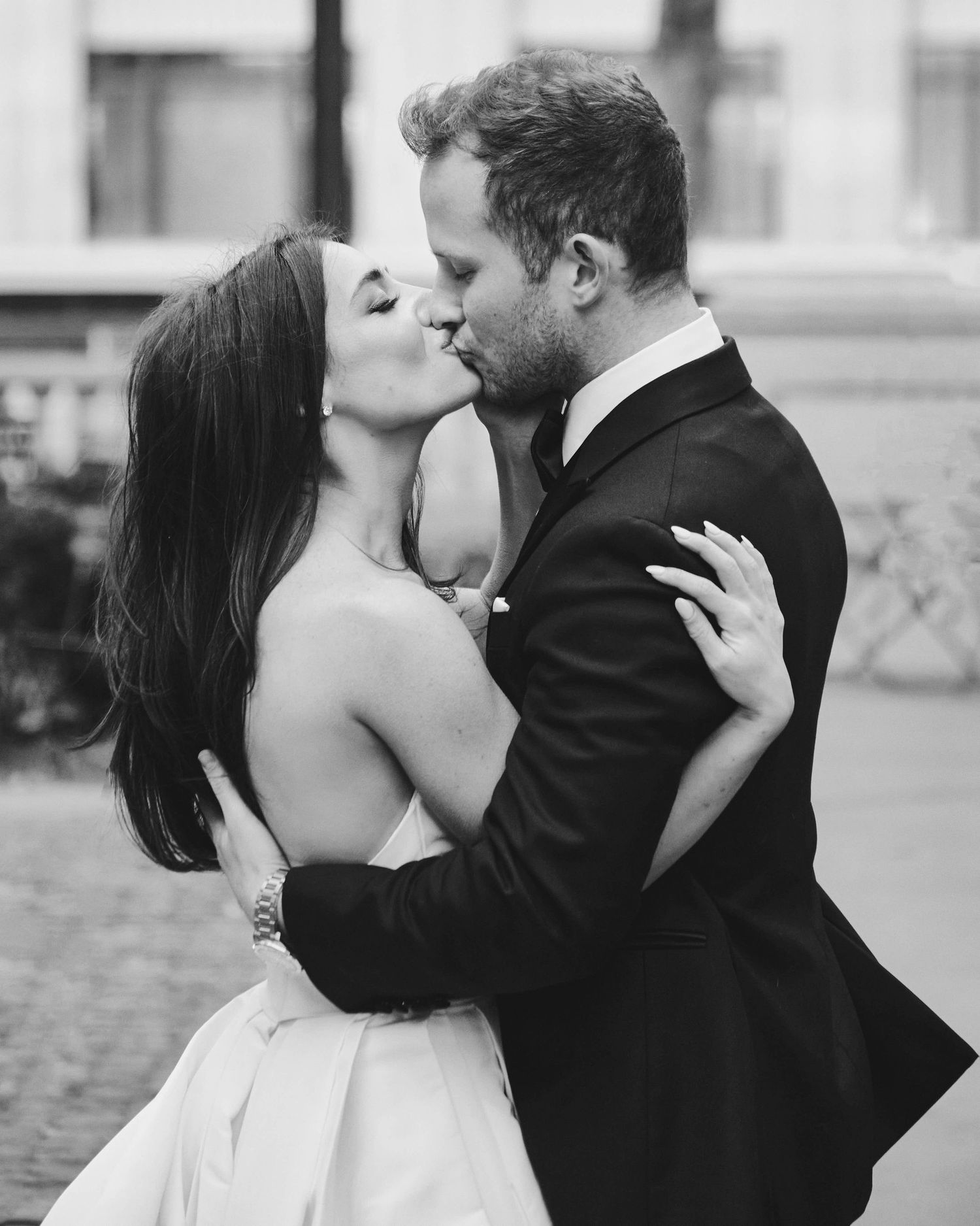Black and white photo of a couple sharing a romantic kiss, bride in strapless gown and groom in dark suit.