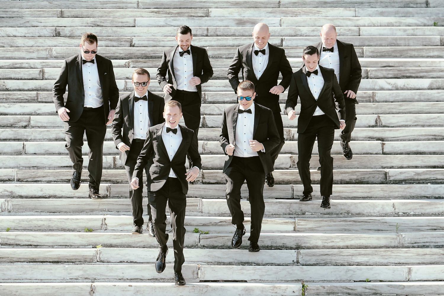 A group in black tuxedos walking down a grand stone staircase in a formal setting.