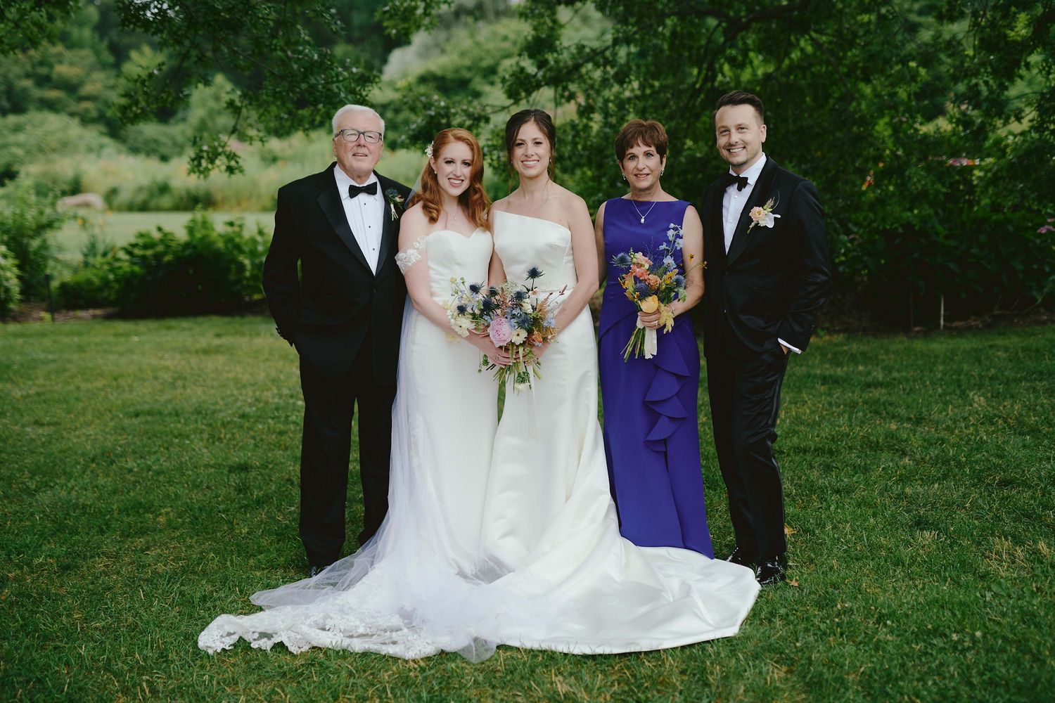 A wedding party in formal attire poses on a lawn, with the bride in white and attendants in purple gowns.