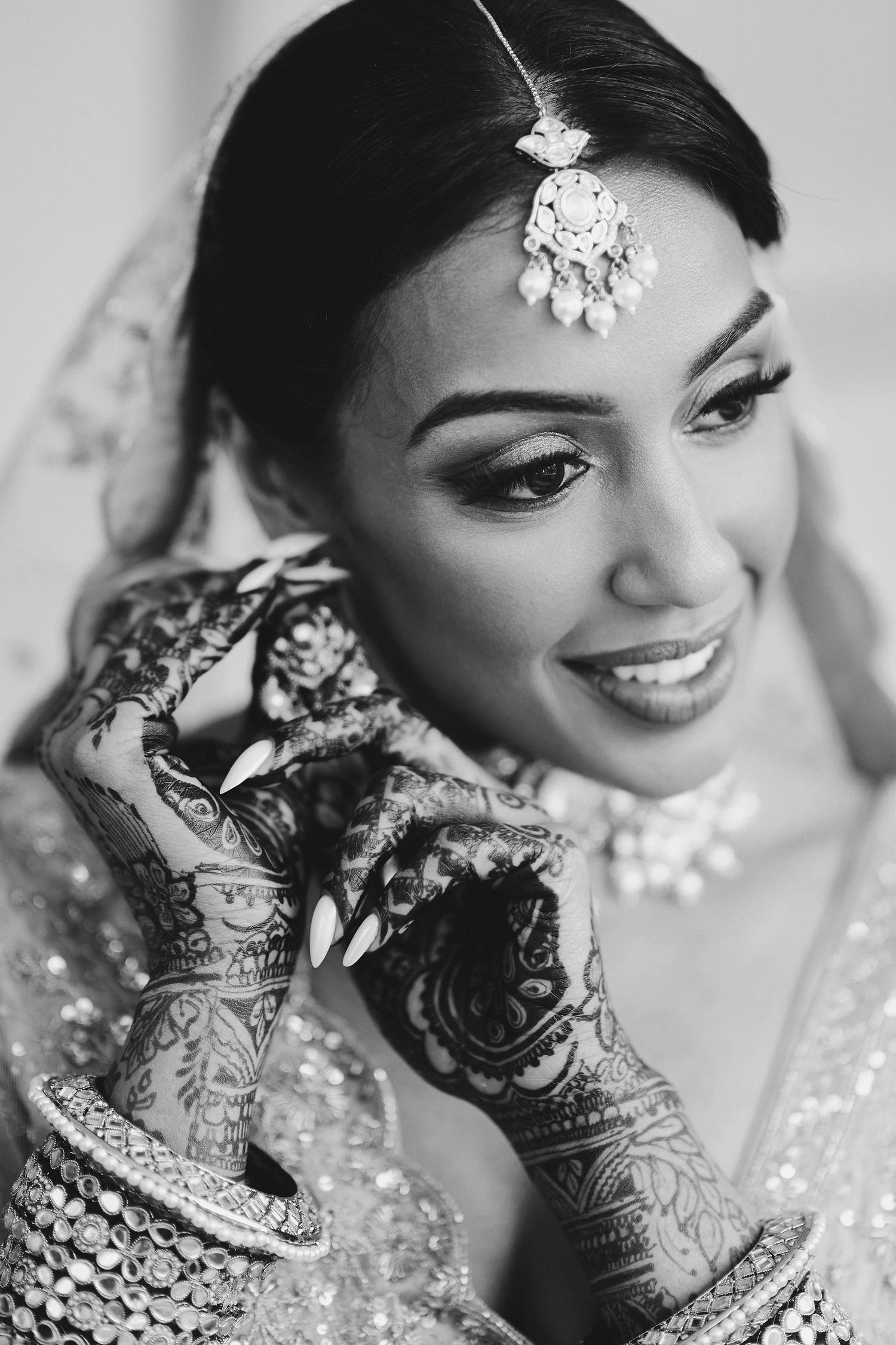 Close-up black and white portrait of traditional Indian bride with ornate henna designs and jewelry.