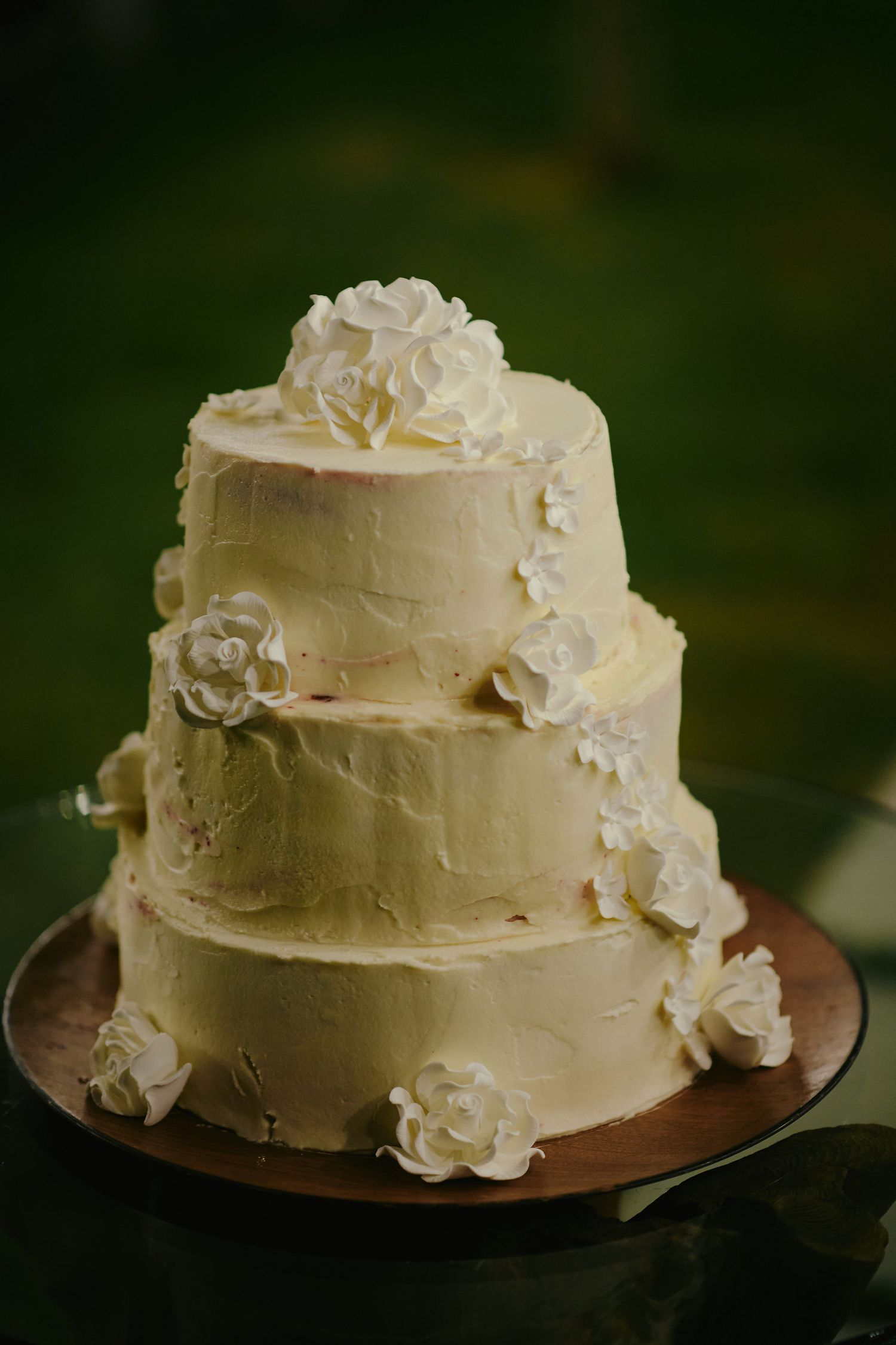 An elegant three-tiered white wedding cake decorated with cream-colored buttercream frosting and delicate sugar roses.