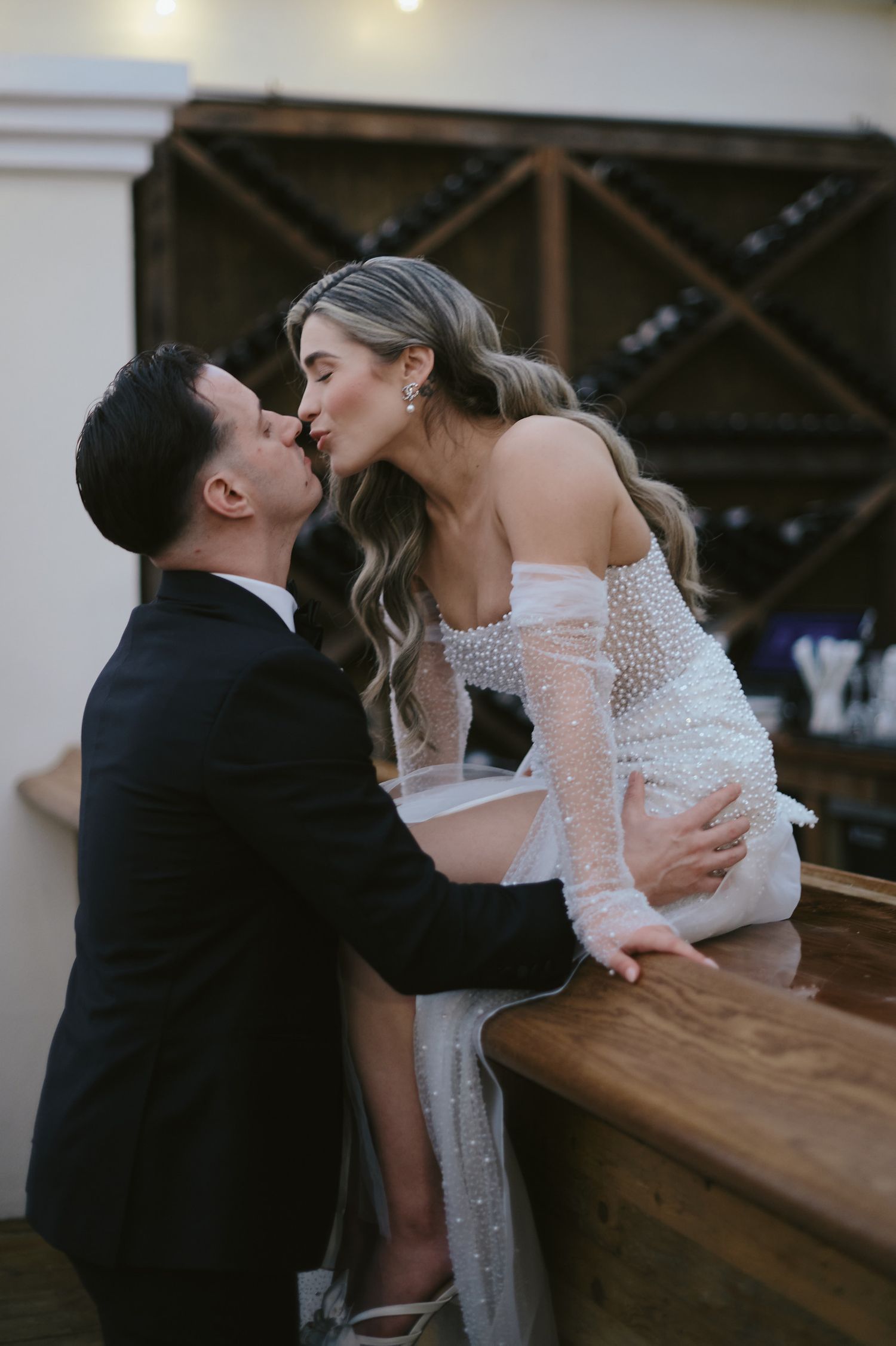 Romantic wedding couple sharing an intimate kiss by rustic wine rack.