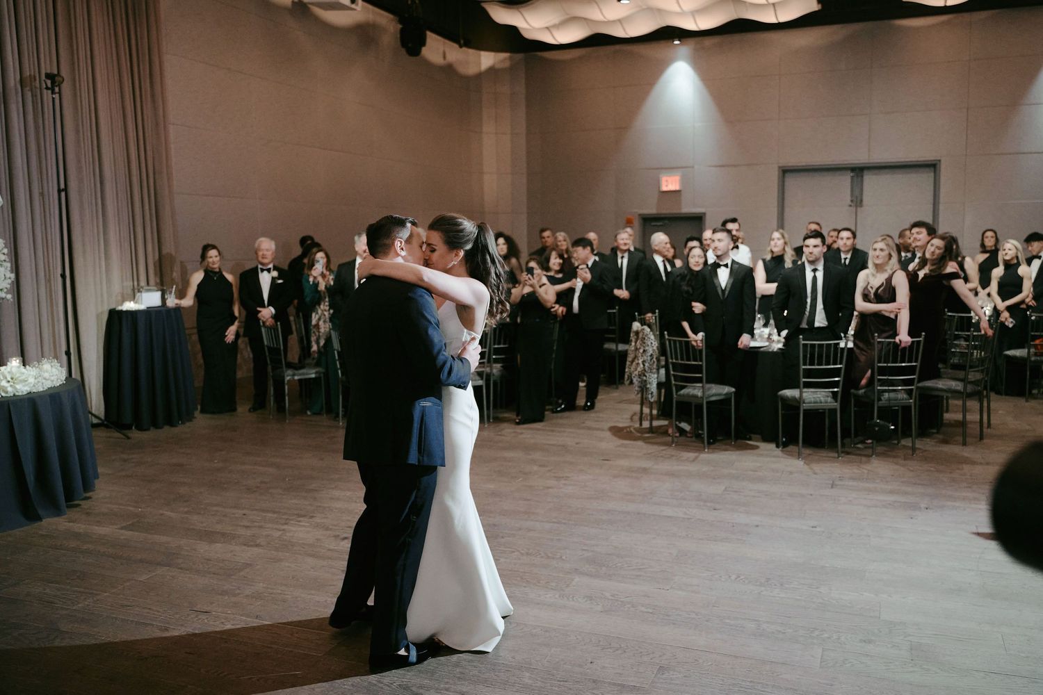 A couple shares their first dance at their wedding reception while guests watch from their tables in the background.
