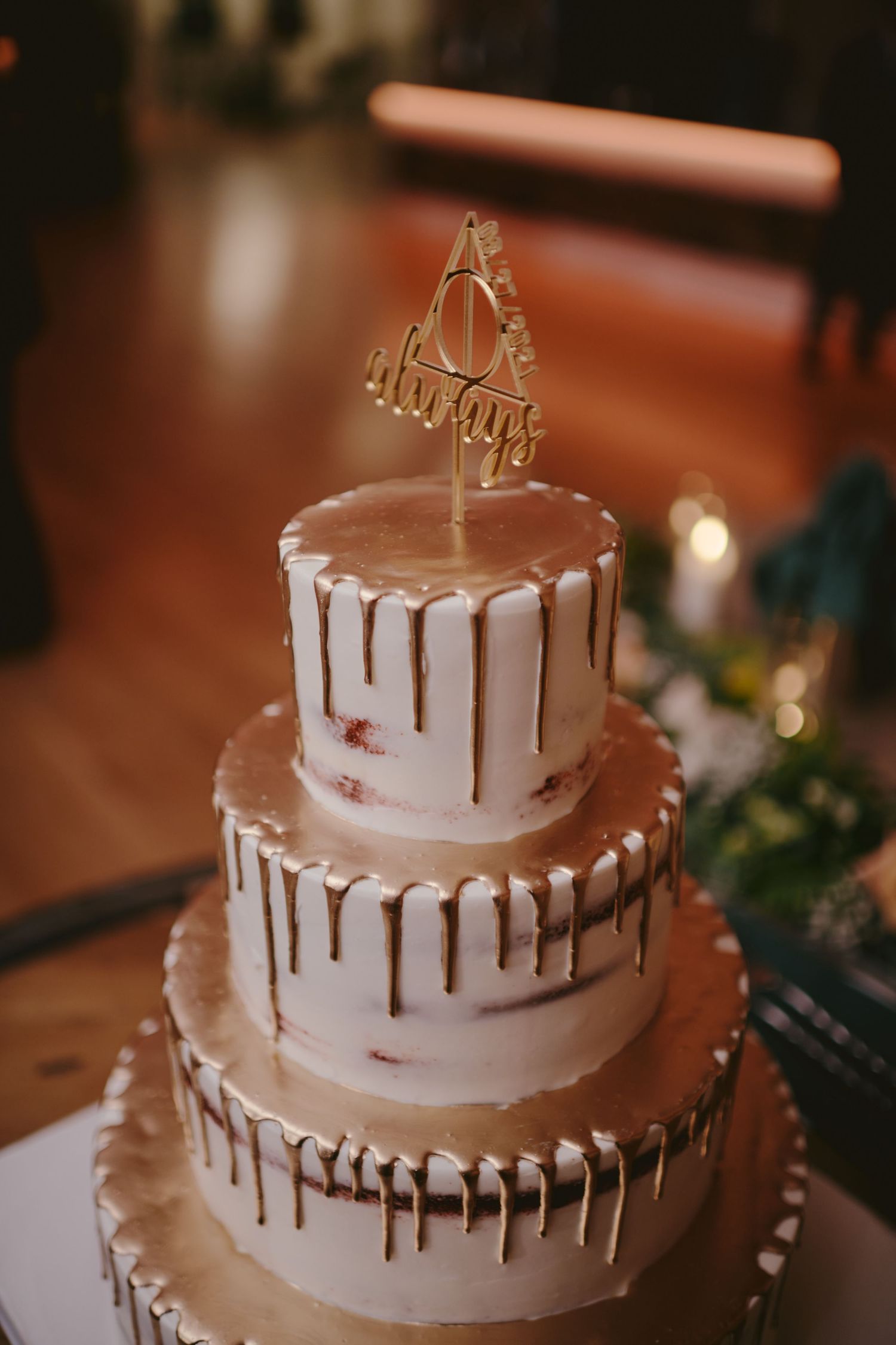 Elegant three-tiered white wedding cake with metallic gold drip details and a delicate gold cake topper for decoration.