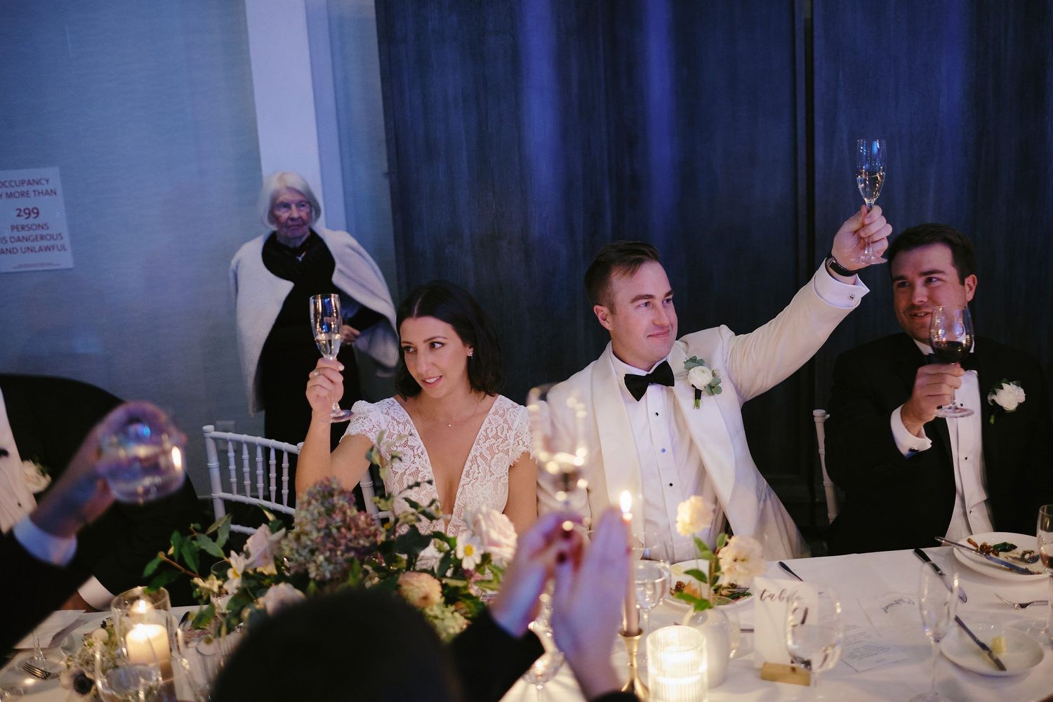 Wedding guests raise their glasses around candlelit tables during an elegant reception celebration.