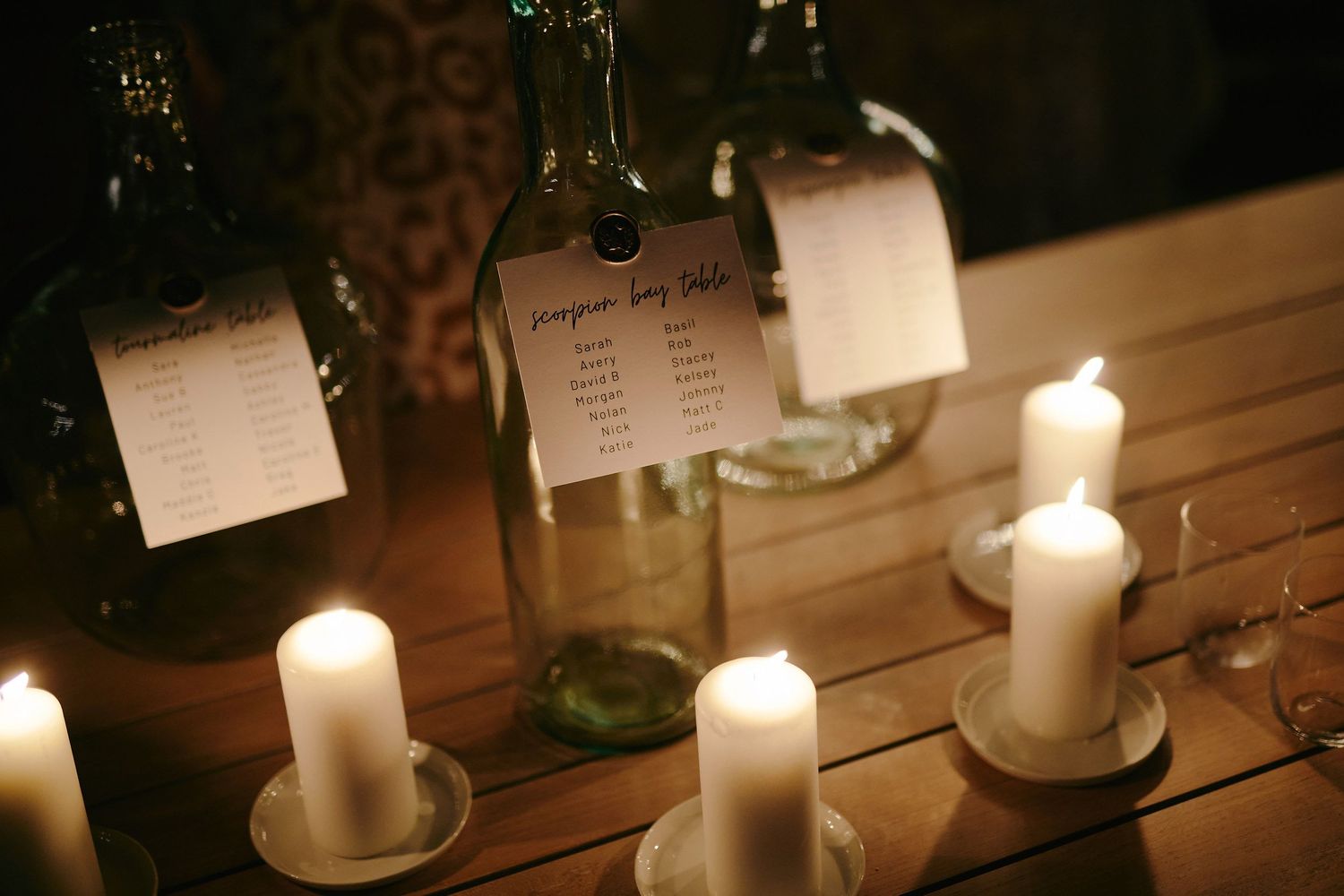Lit white candles and vintage glass bottles with paper notes on a rustic wooden table create an atmospheric setting.