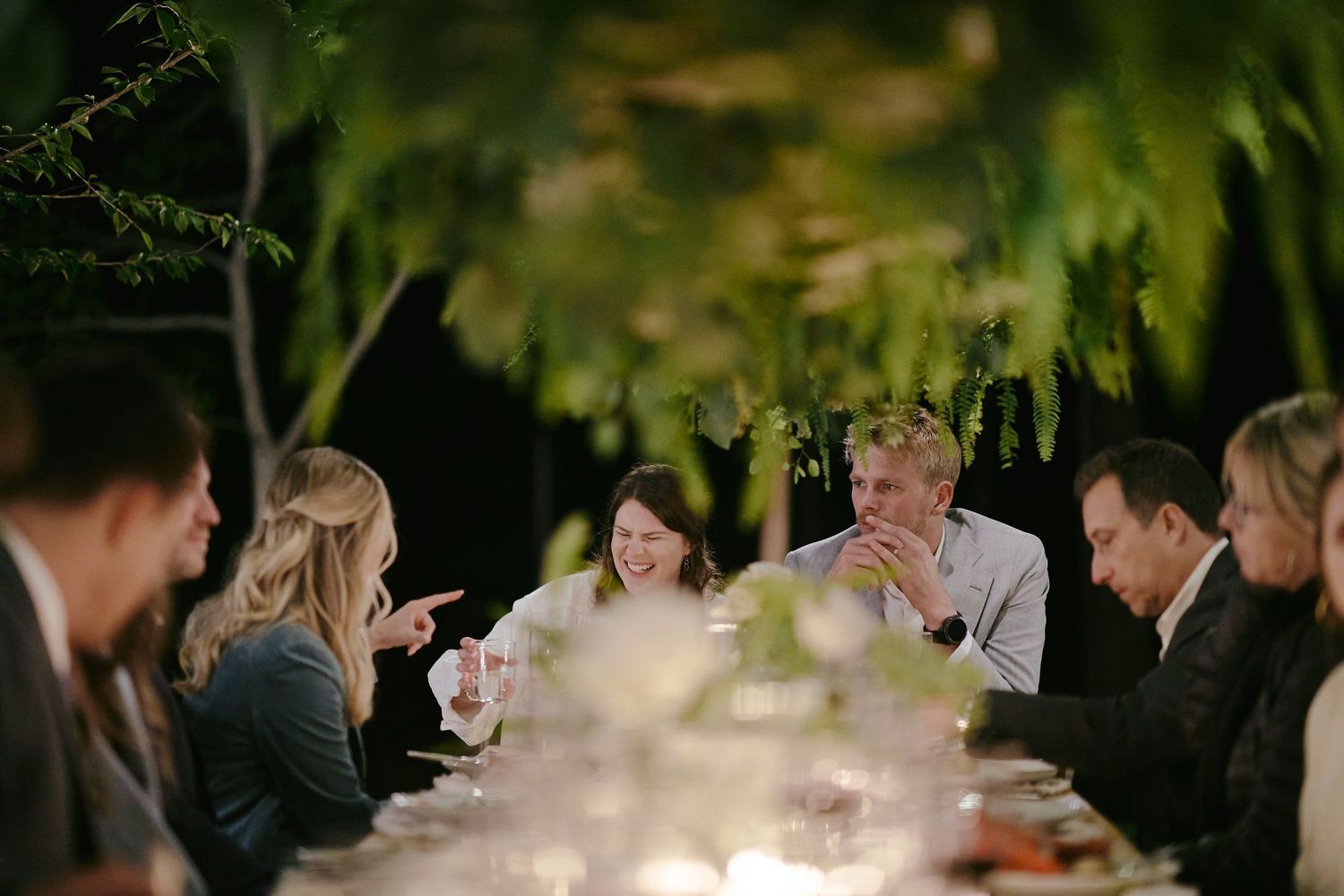 People gathered around an outdoor dining table at dusk enjoying conversation under ambient lighting.
