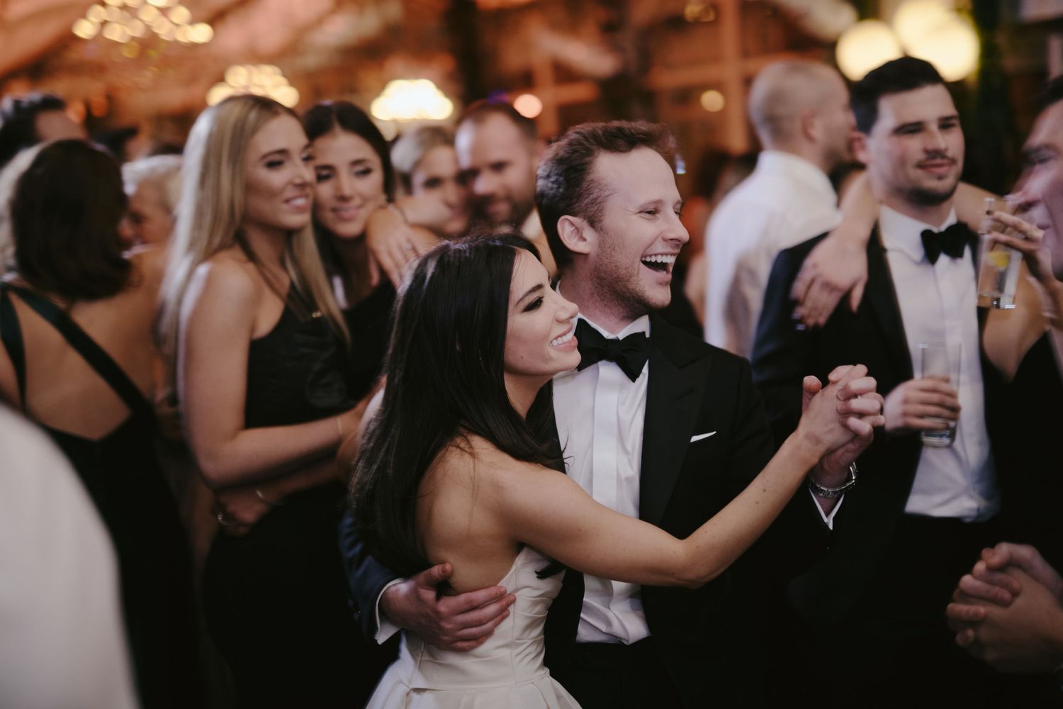 Wedding guests dance and laugh together on a lively dance floor at an elegant evening reception.