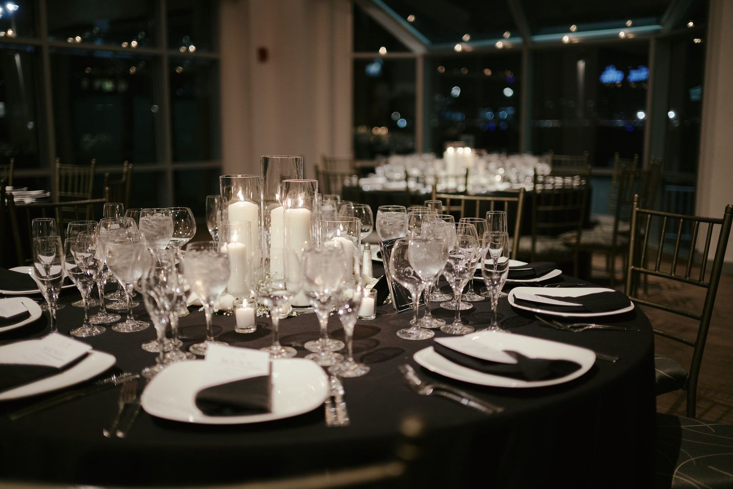 Elegant black and white table setting at night with glowing candles and crystal glassware for formal dining.