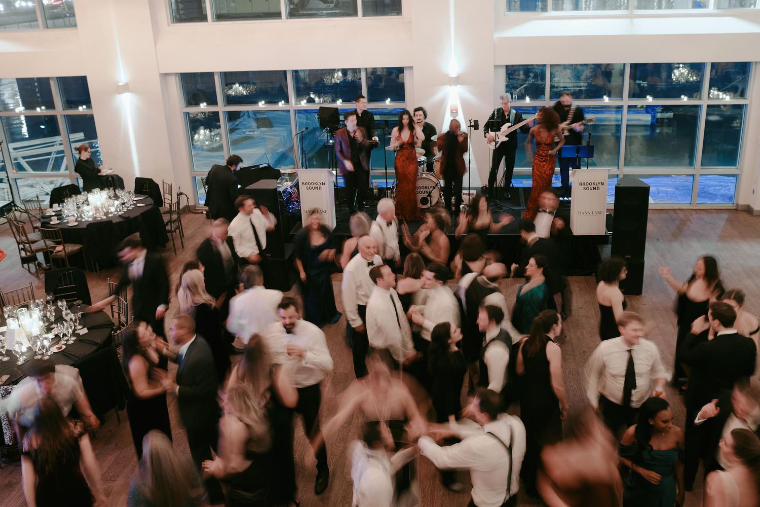 A crowded dance floor at an indoor reception venue with party guests dancing under bright lighting.