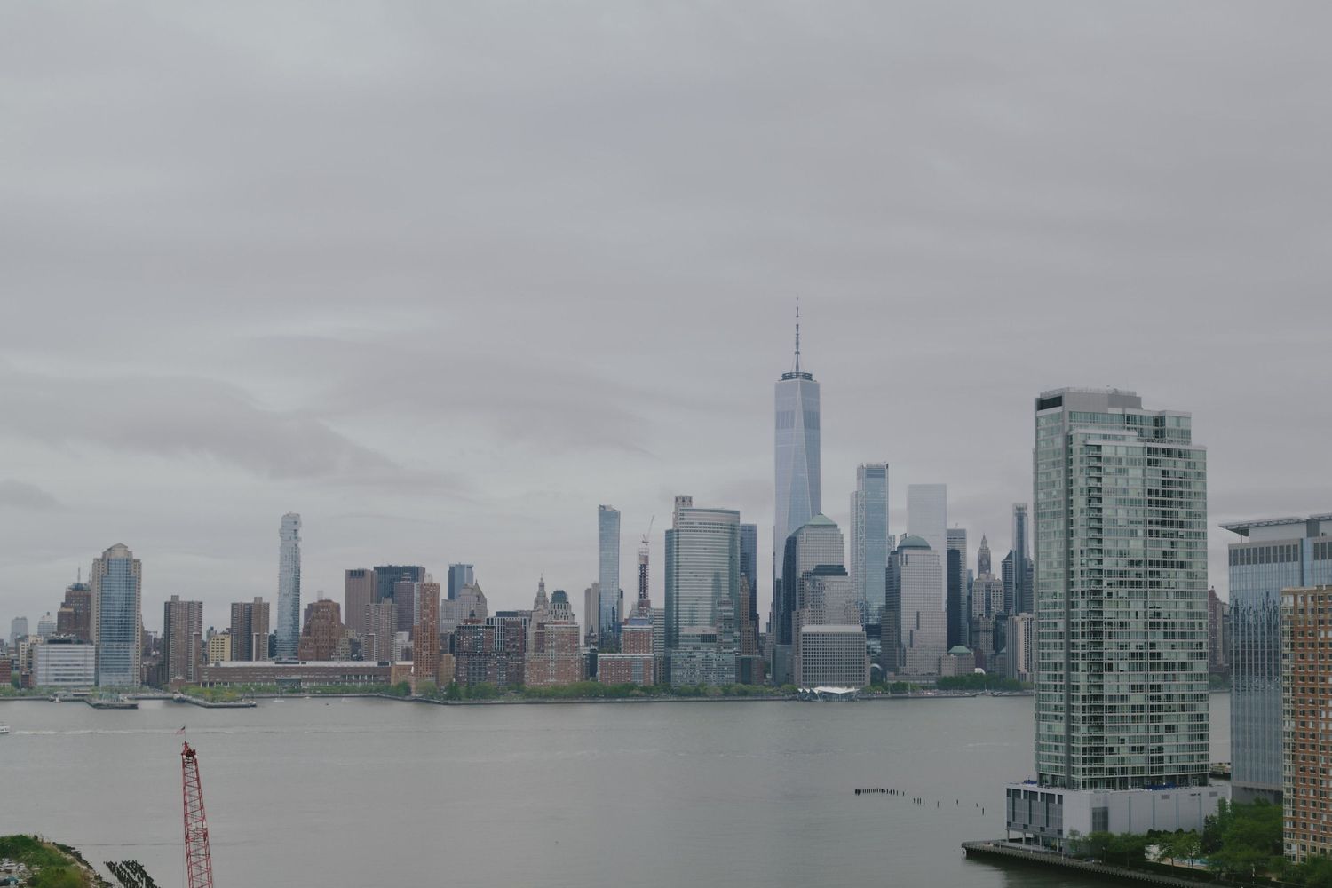 View of downtown Manhattan skyline with One World Trade Center and surrounding skyscrapers on a cloudy day.