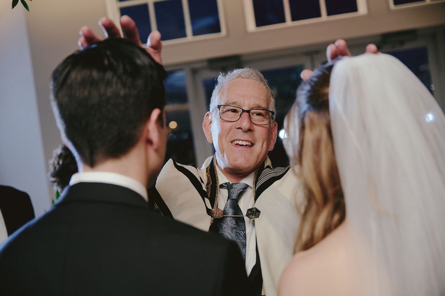 A joyful person in glasses shares a candid moment with a couple at their wedding ceremony.