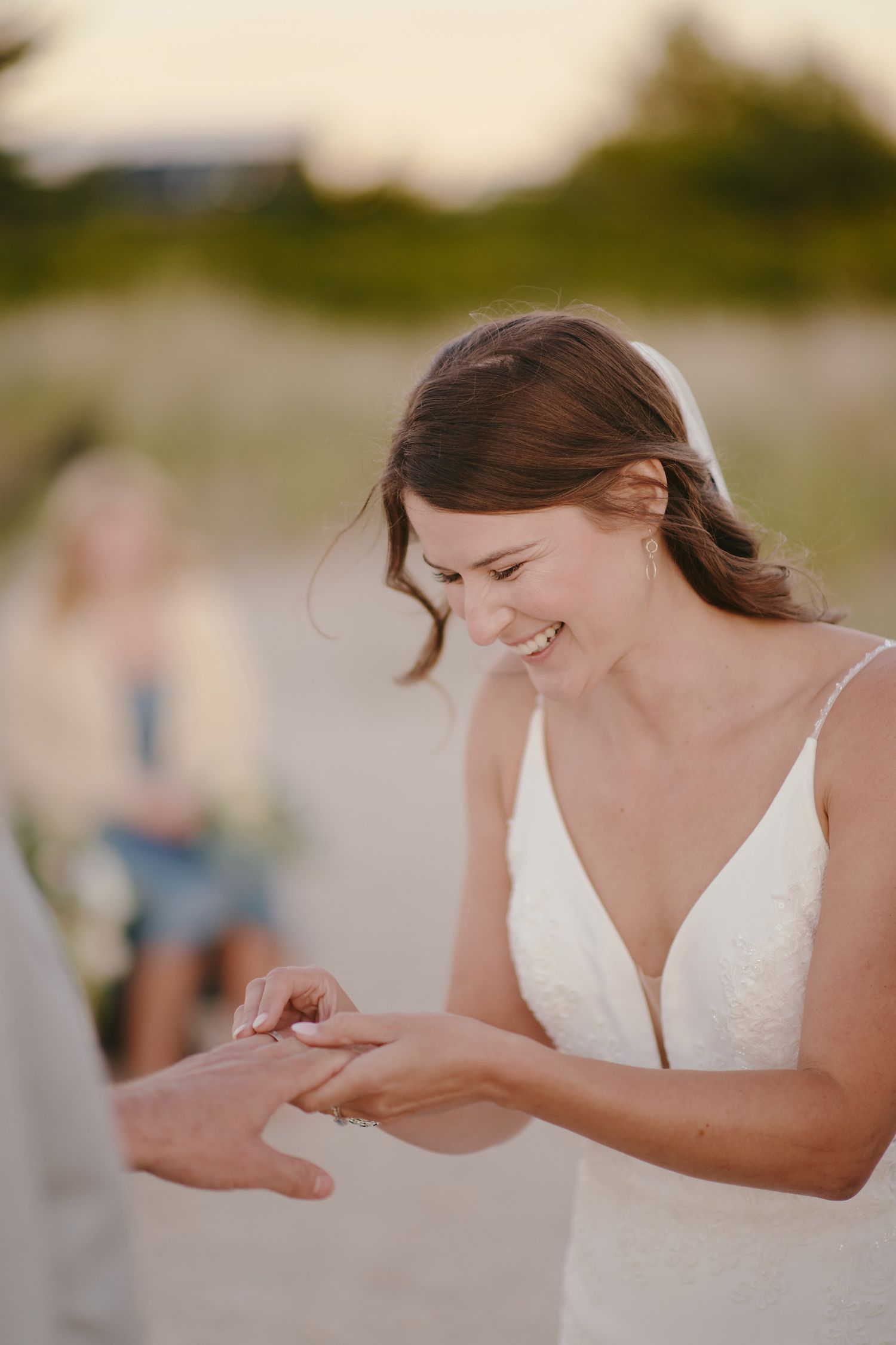 A joyful moment during a beachside wedding ceremony as a bride in white places a ring on their partner's hand.