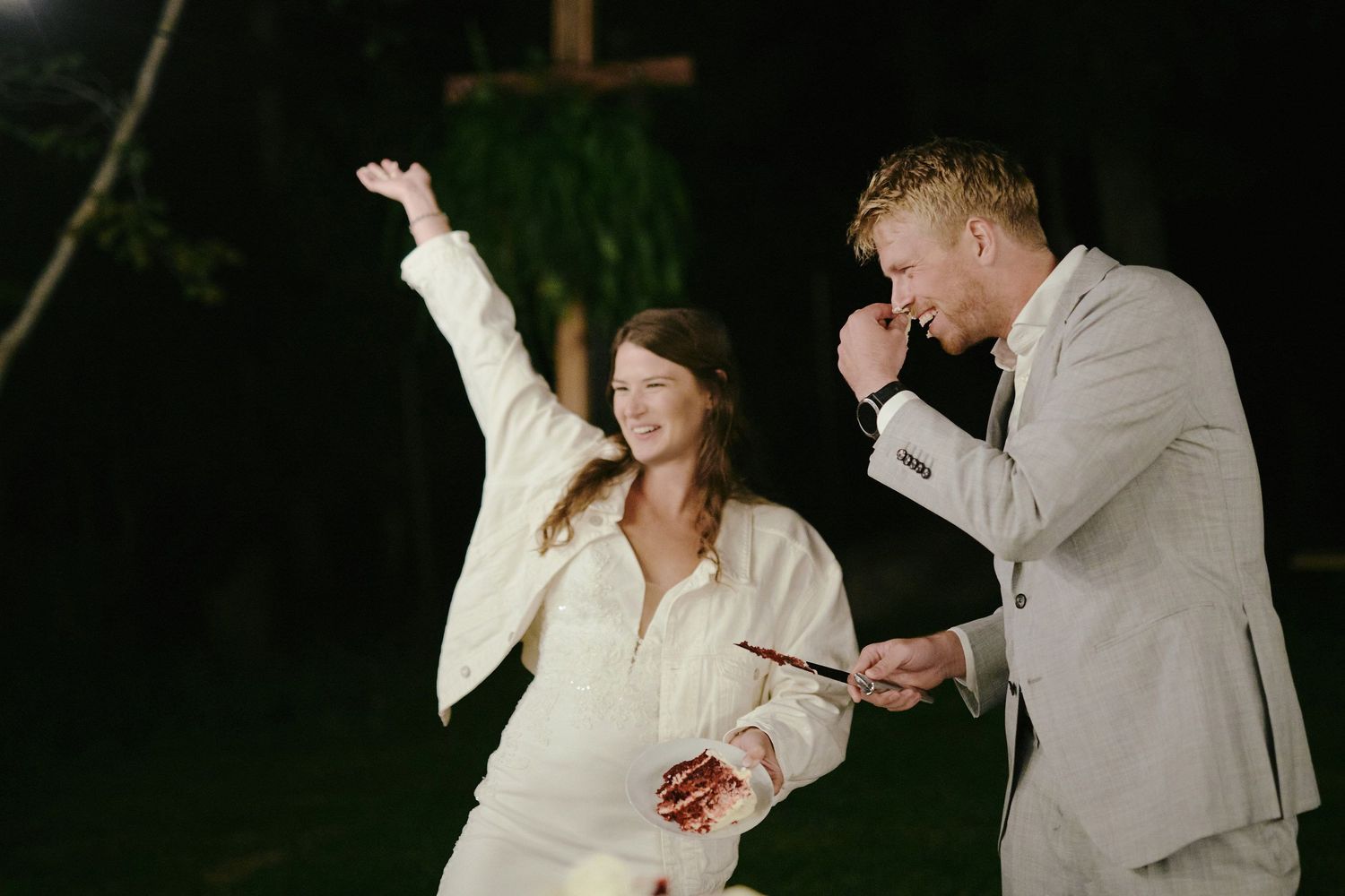 Two people dancing and singing energetically together in formal white and beige outfits during a nighttime celebration.