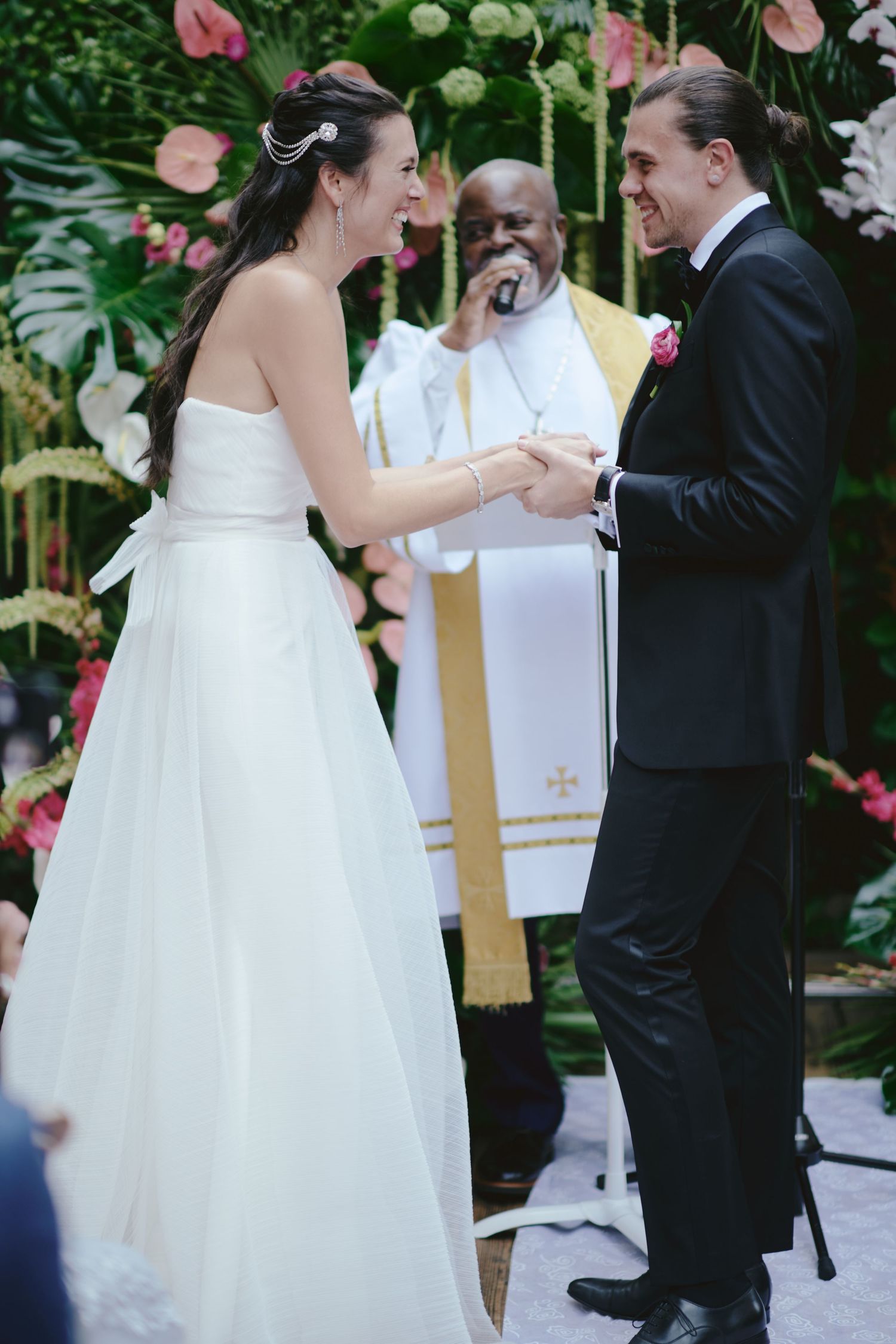 A joyful moment during a wedding ceremony with pink floral decorations and a lush green backdrop.