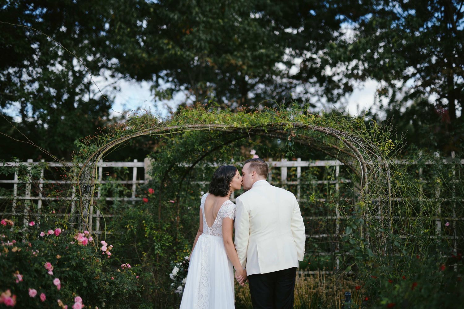 A couple shares a romantic moment in a garden with white trellis arches and blooming roses.