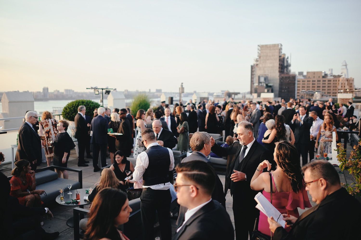 A crowded rooftop party overlooking New York City with guests mingling during an elegant evening event.