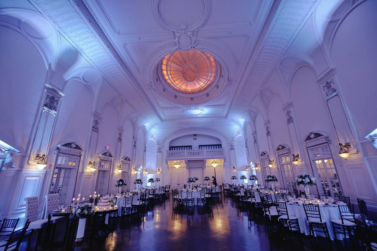 Elegant white ballroom with grand lighting fixtures and formal table settings prepared for an upscale wedding reception.