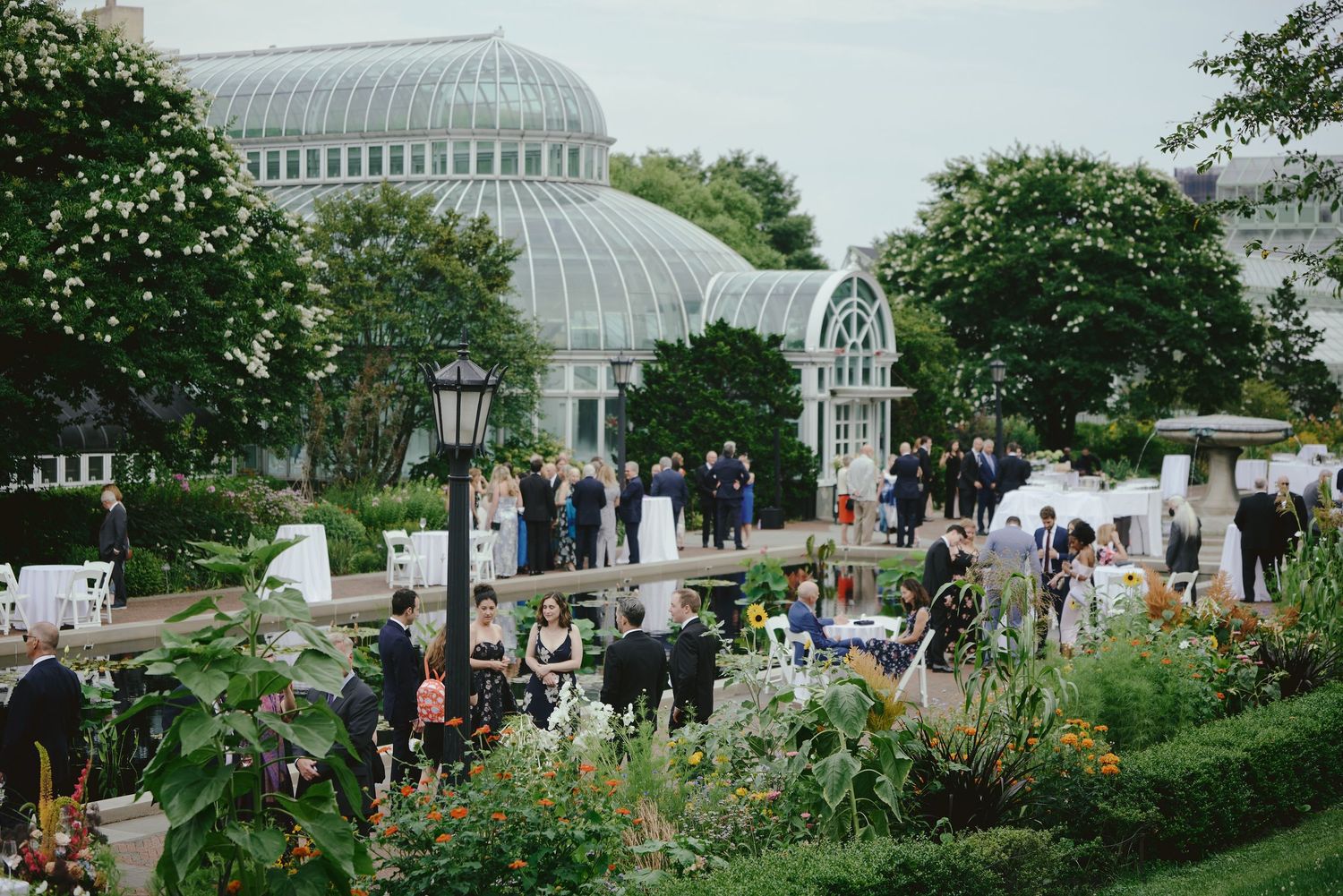 Elegant outdoor wedding reception at a botanical garden greenhouse venue with lush greenery and guests mingling.