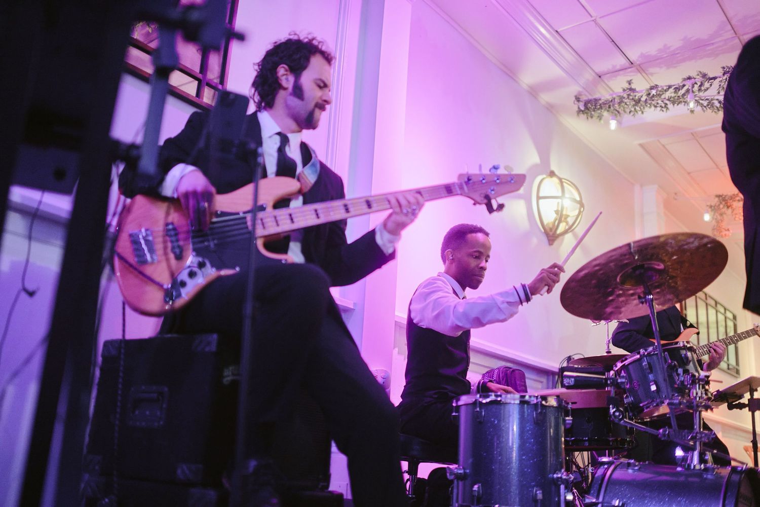 Musicians perform on stage with guitar and drums under purple lighting at a live music venue.