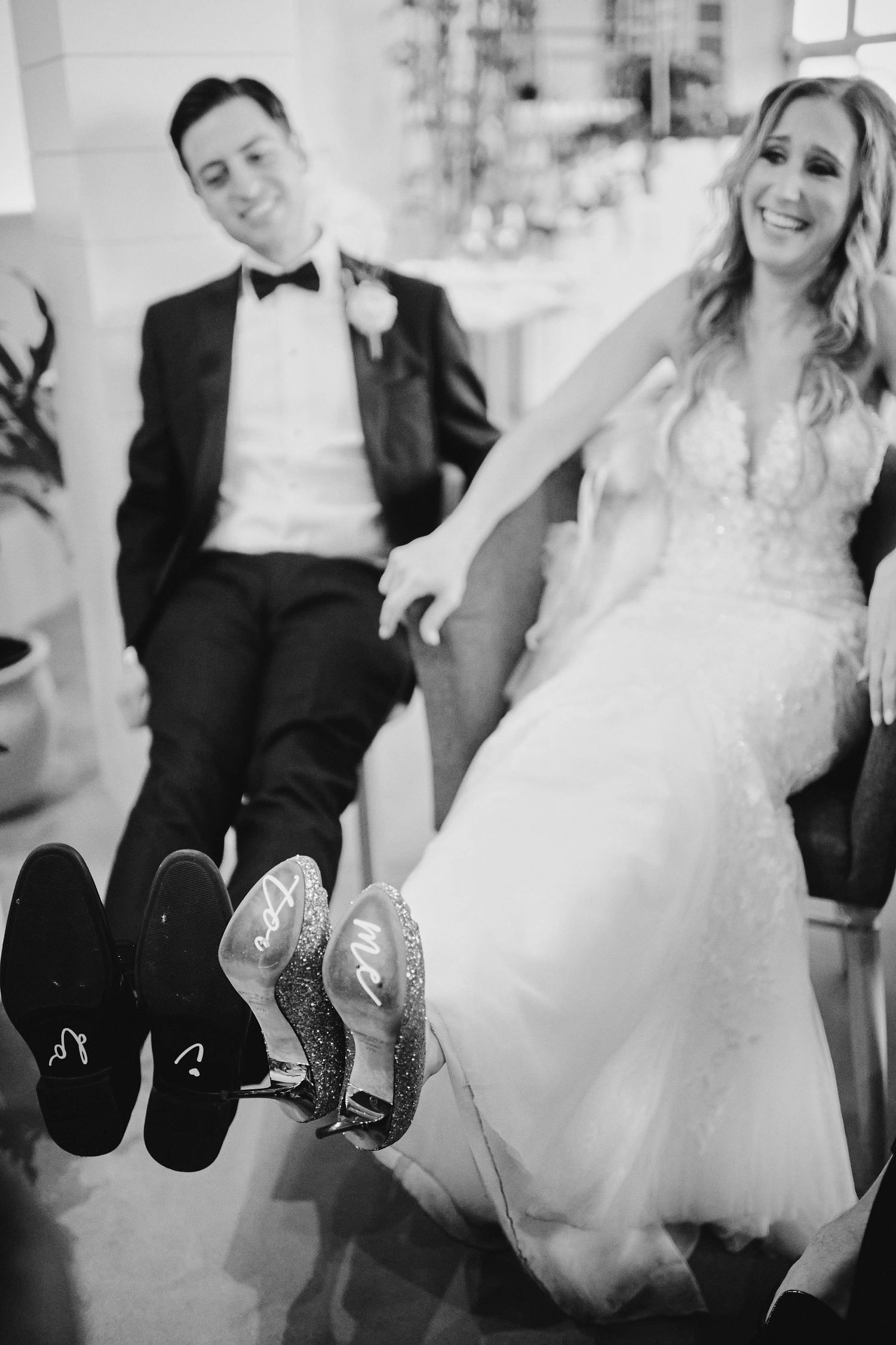 Black and white wedding photo showing couple sitting with their shoes displayed, featuring dress shoes and high heels.