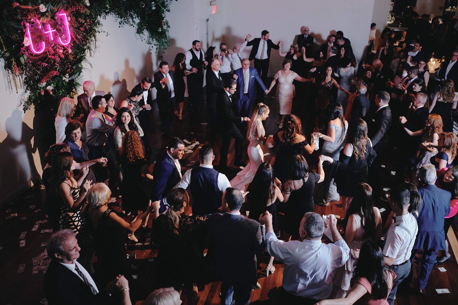 A lively dance floor filled with wedding reception guests dancing and celebrating under dim lighting and floral decorations.